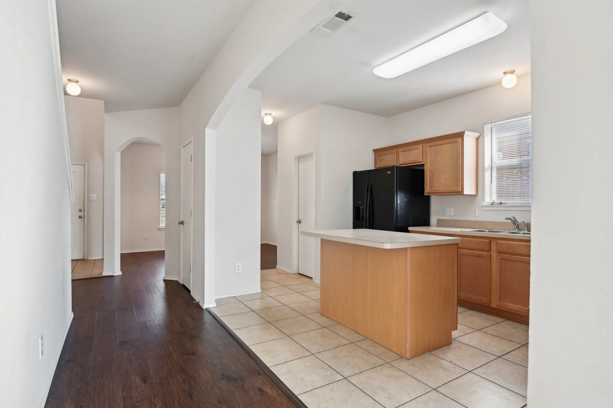 Kitchen featuring black fridge, a healthy amount of sunlight, a kitchen island, and light tile patterned floors