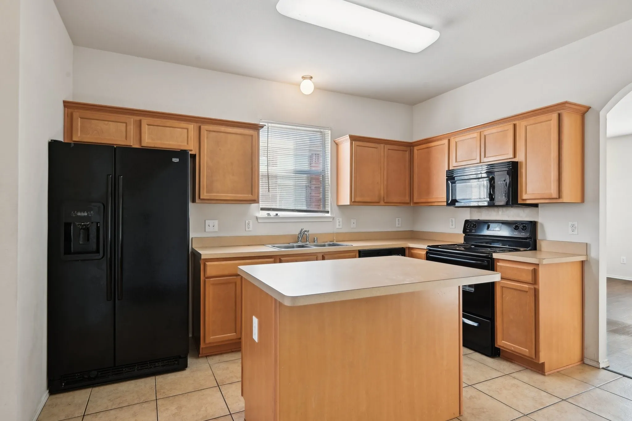 Kitchen featuring light tile patterned flooring, a center island, sink, and black appliances