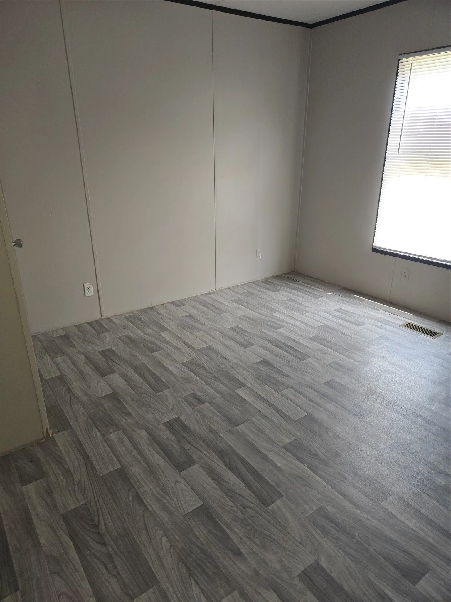 Room with wood-finish flooring, light-toned wall panels, and a window with horizontal blinds