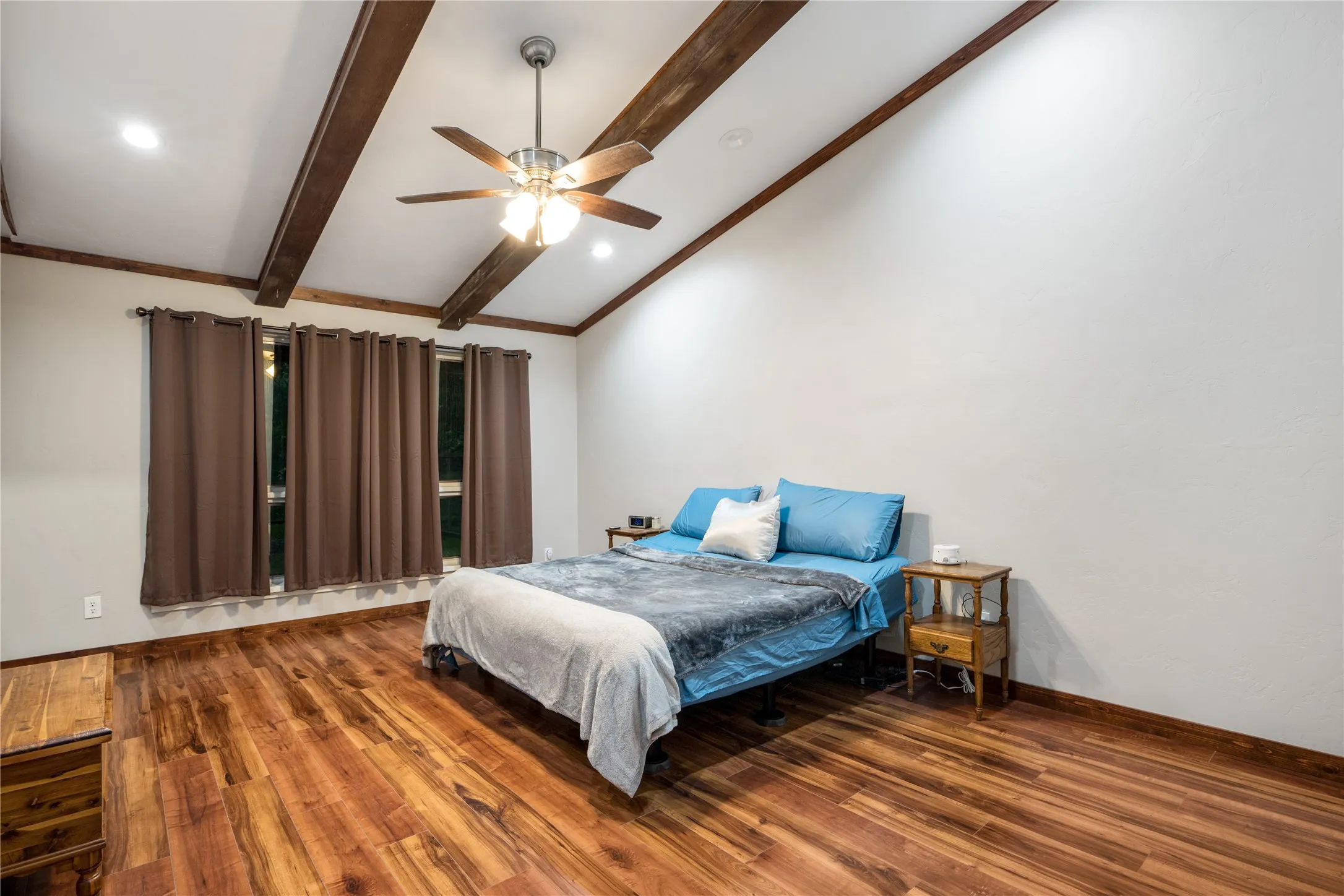 Vaulted white ceilings with exposed wood beams, wood-finish flooring, recessed lighting, and a ceiling fan with light fixture