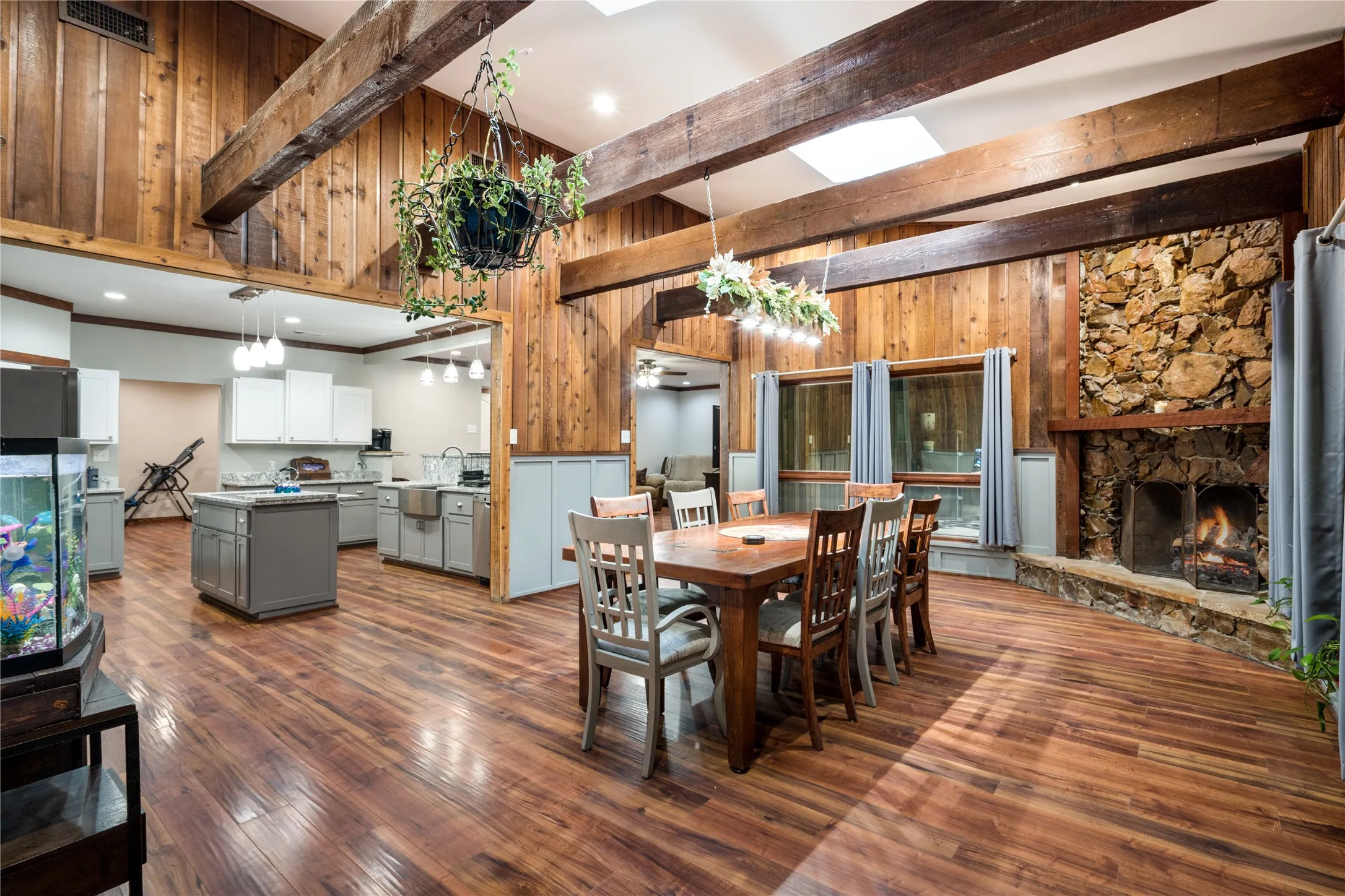 Expansive interior featuring high vaulted ceilings with exposed wood beams, a stone fireplace, wood-finish flooring, and natural wood paneling
