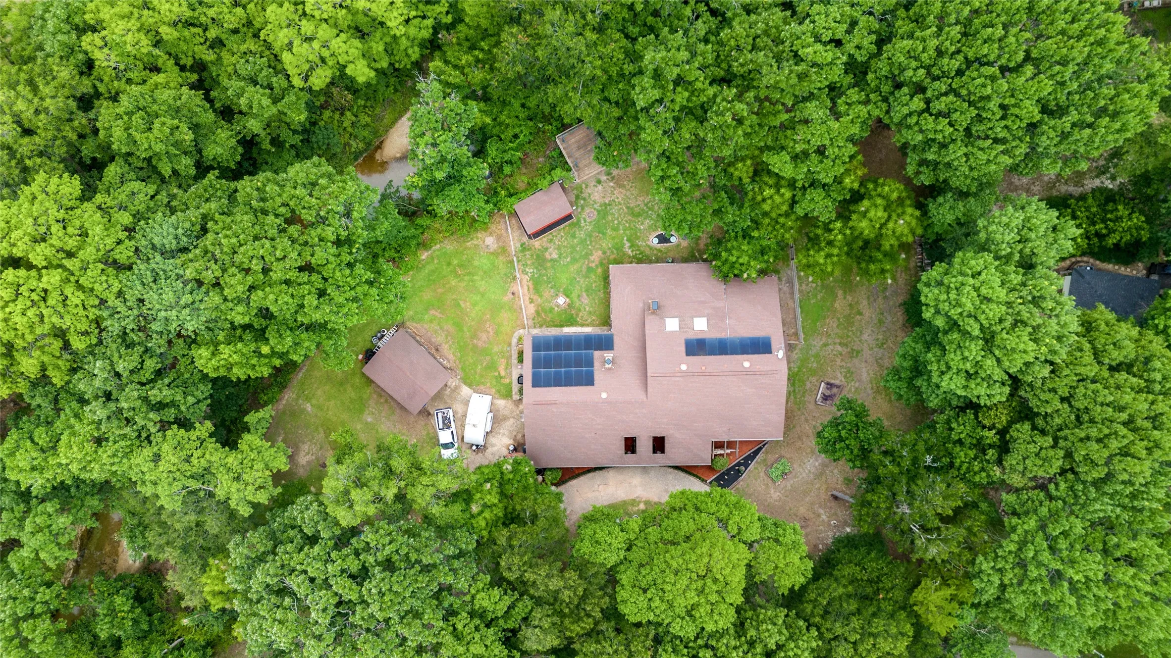 Private wooded lot featuring a residence with a brown shingle roof and multiple solar panel installations