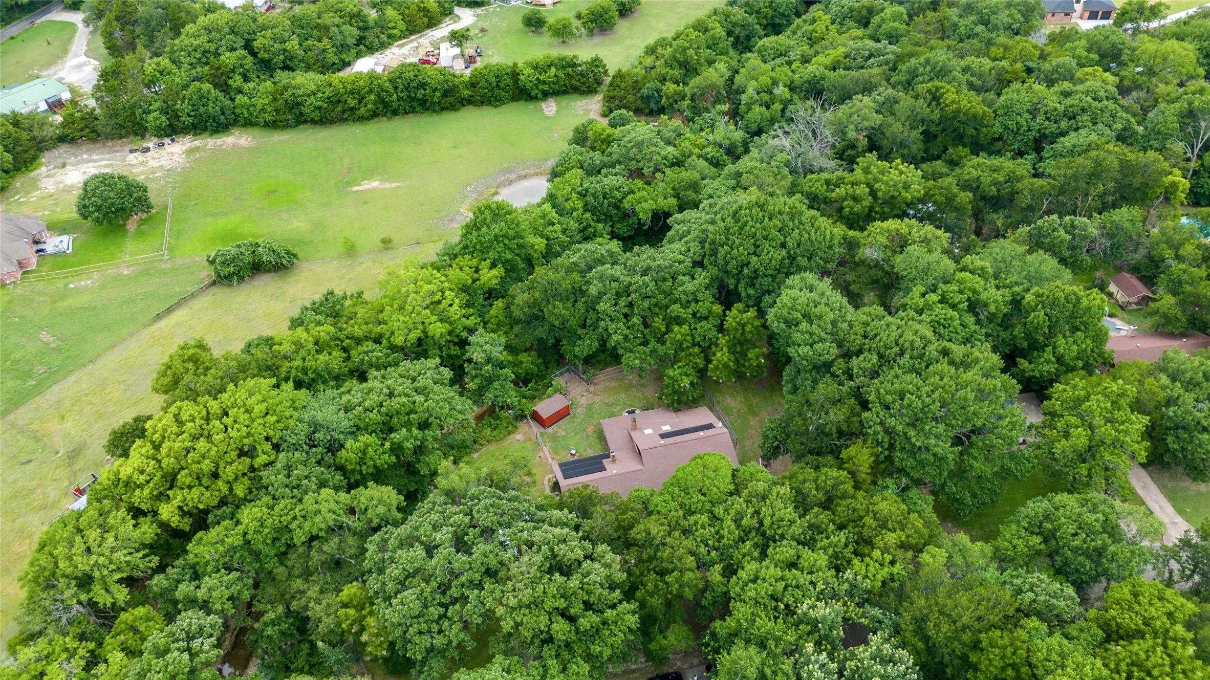 Expansive property surrounded by mature trees, featuring a brown-roofed residence, a separate brown outbuilding, and a red-roofed shed