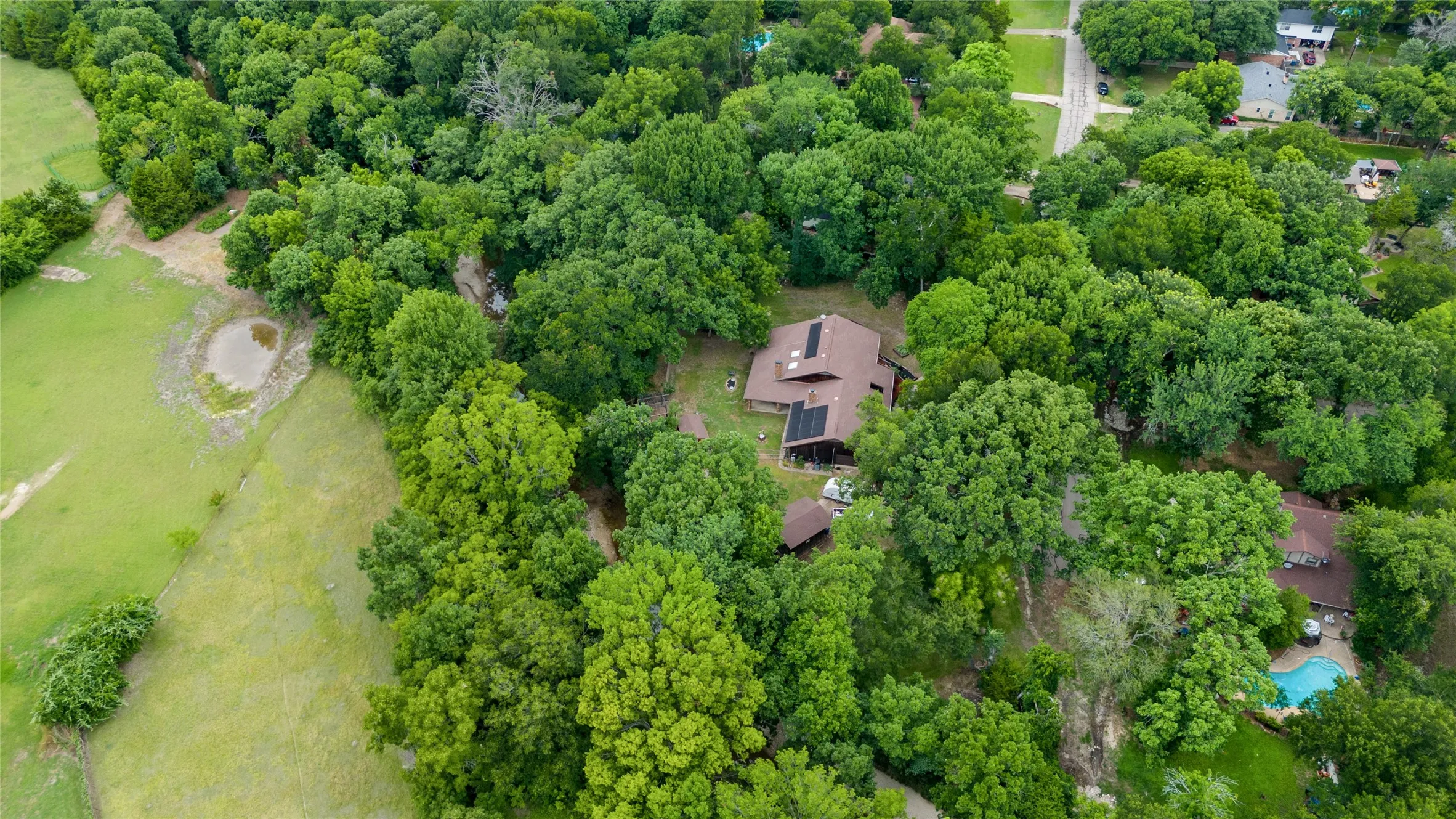 Expansive property featuring a brown roofline, solar panels, and a surrounding canopy of mature trees