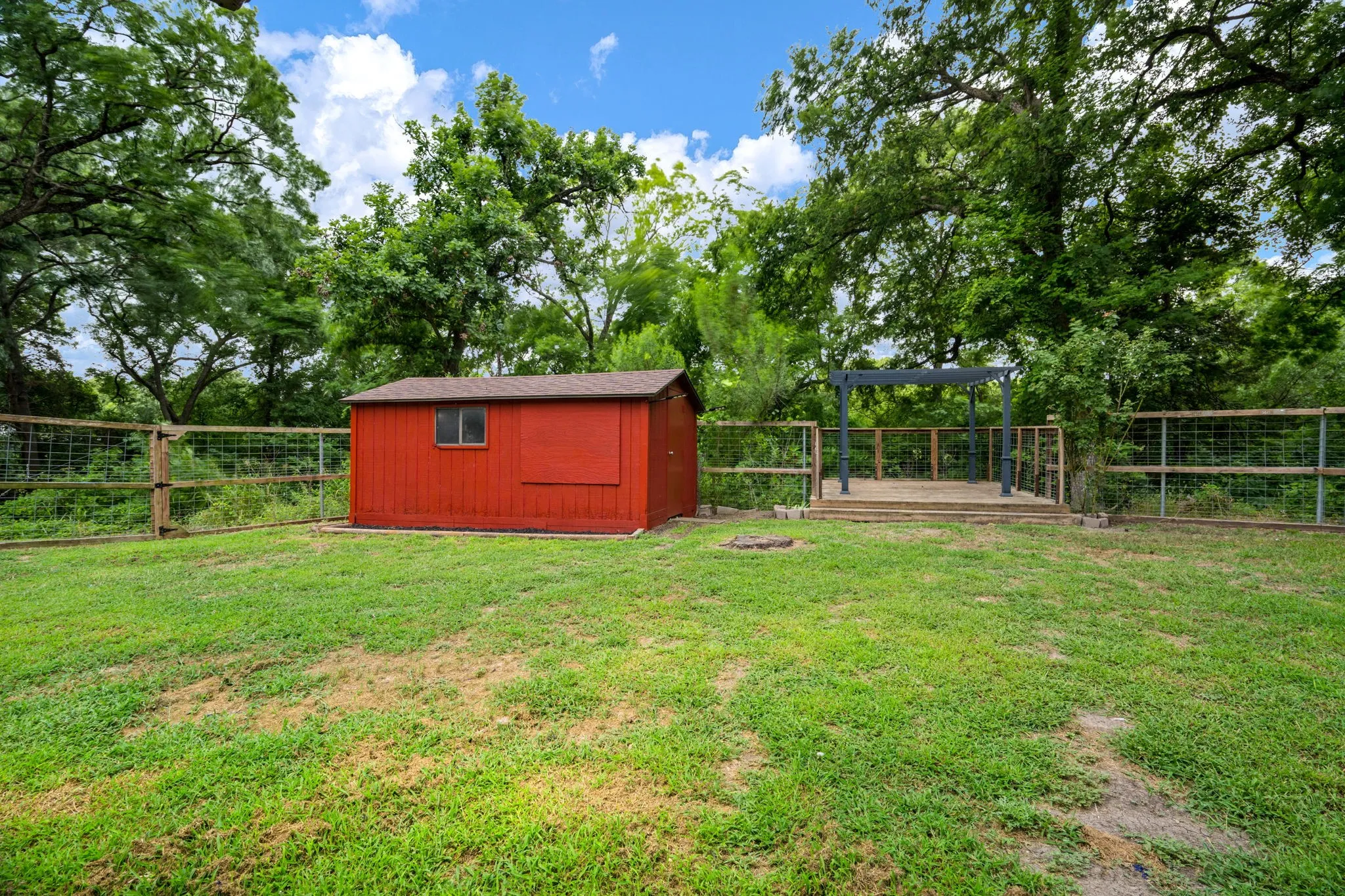 Expansive backyard featuring a red storage shed, a wood-decked patio with an open pergola, and perimeter fencing