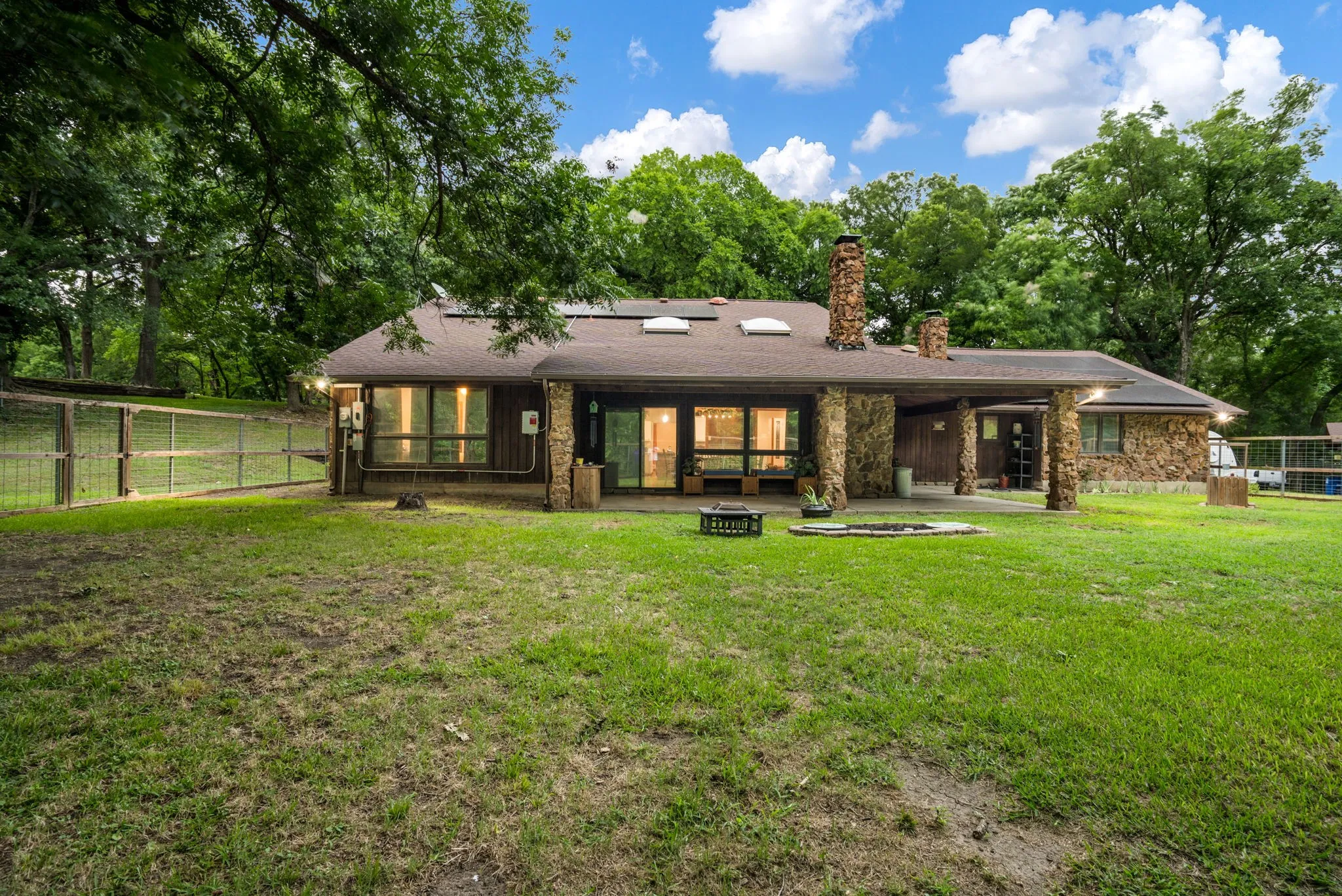 Expansive backyard featuring a stone-clad exterior, multiple skylights, a stone chimney, and a covered patio area