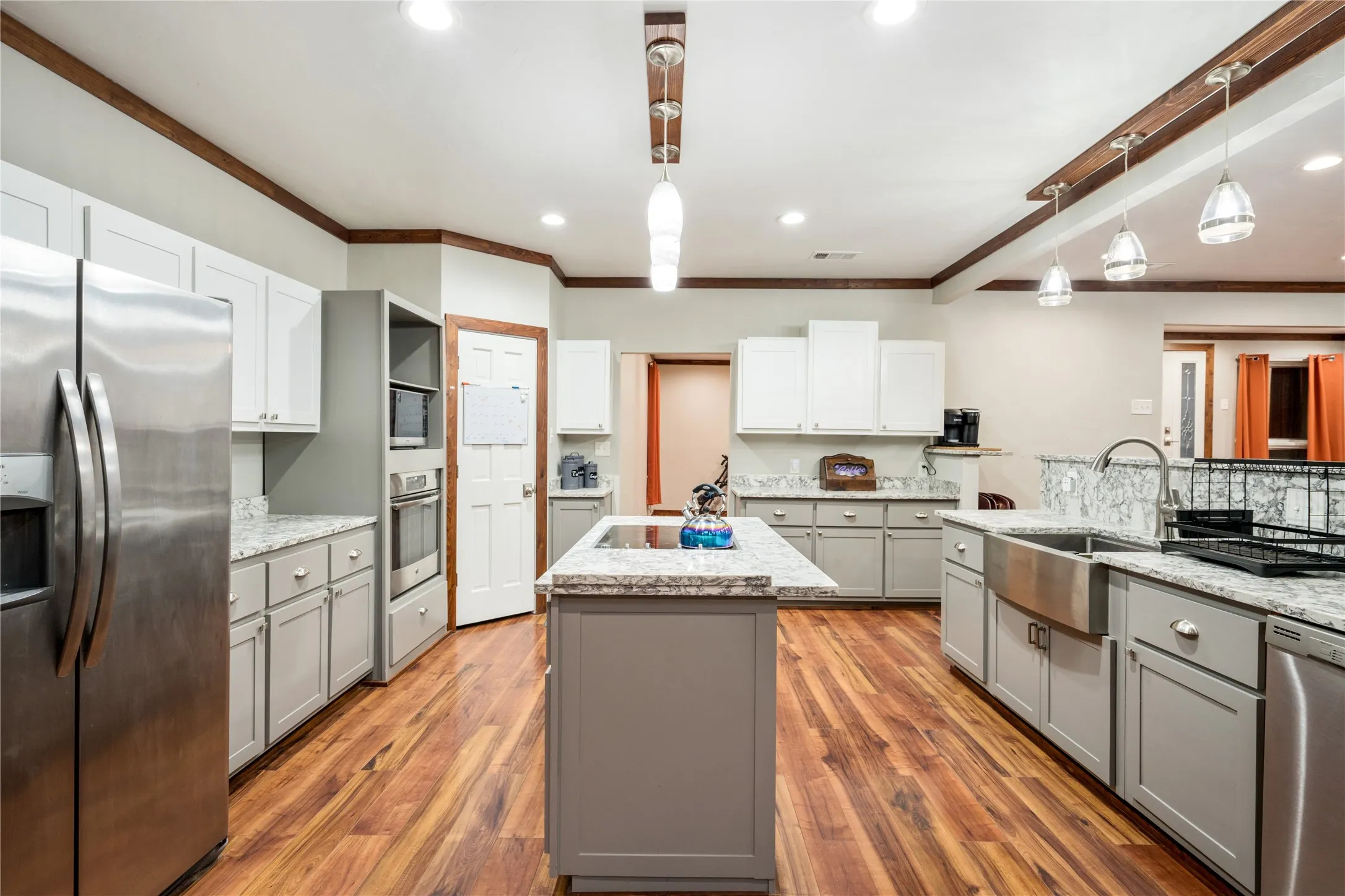 Spacious kitchen featuring wood-finish flooring, light grey and white cabinetry, stone countertops, stainless steel appliances, and a central island with a built-in cooktop