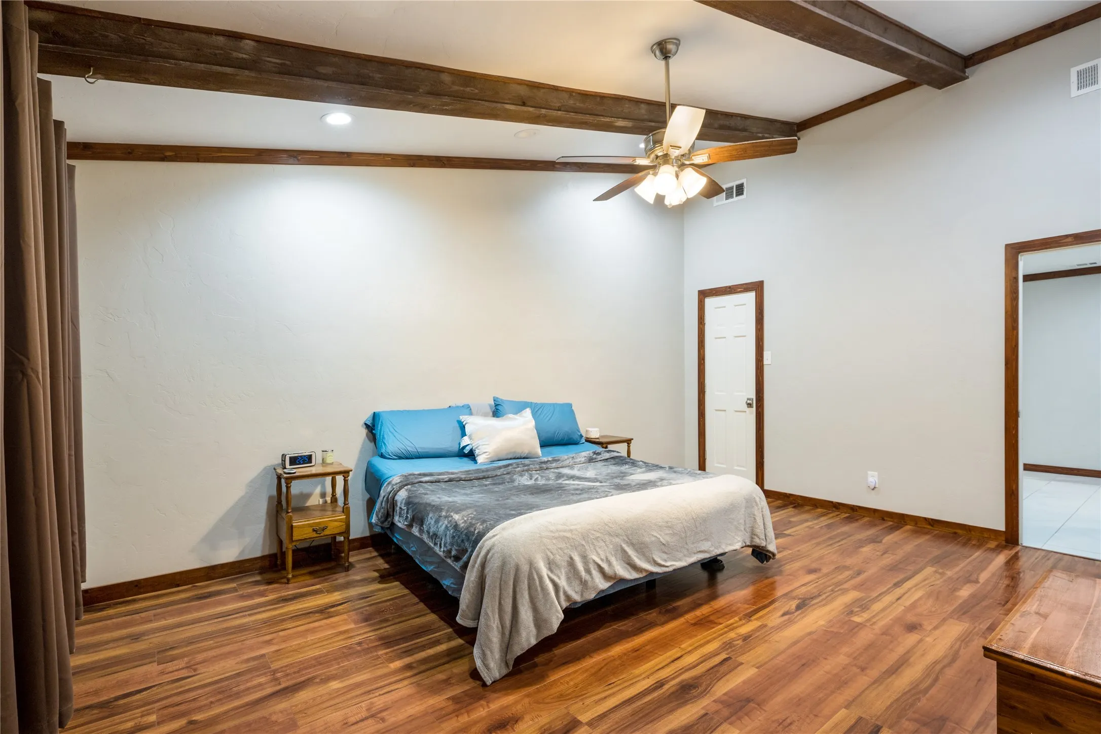 Spacious room featuring wood-finish flooring, vaulted ceilings with exposed wood beams, a ceiling fan with integrated lighting, and recessed overhead lighting