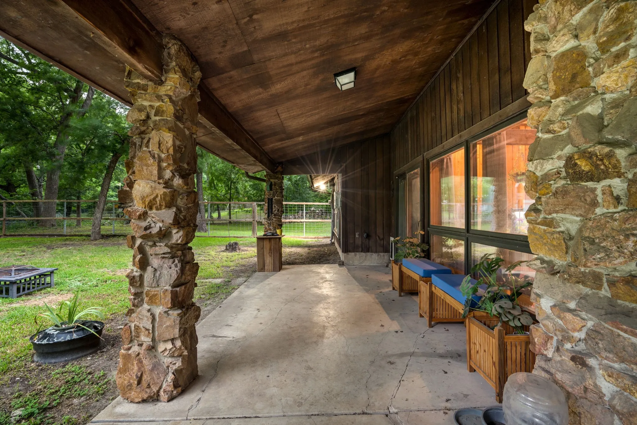 Covered concrete patio featuring stone columns, wood-paneled walls, and large window panels