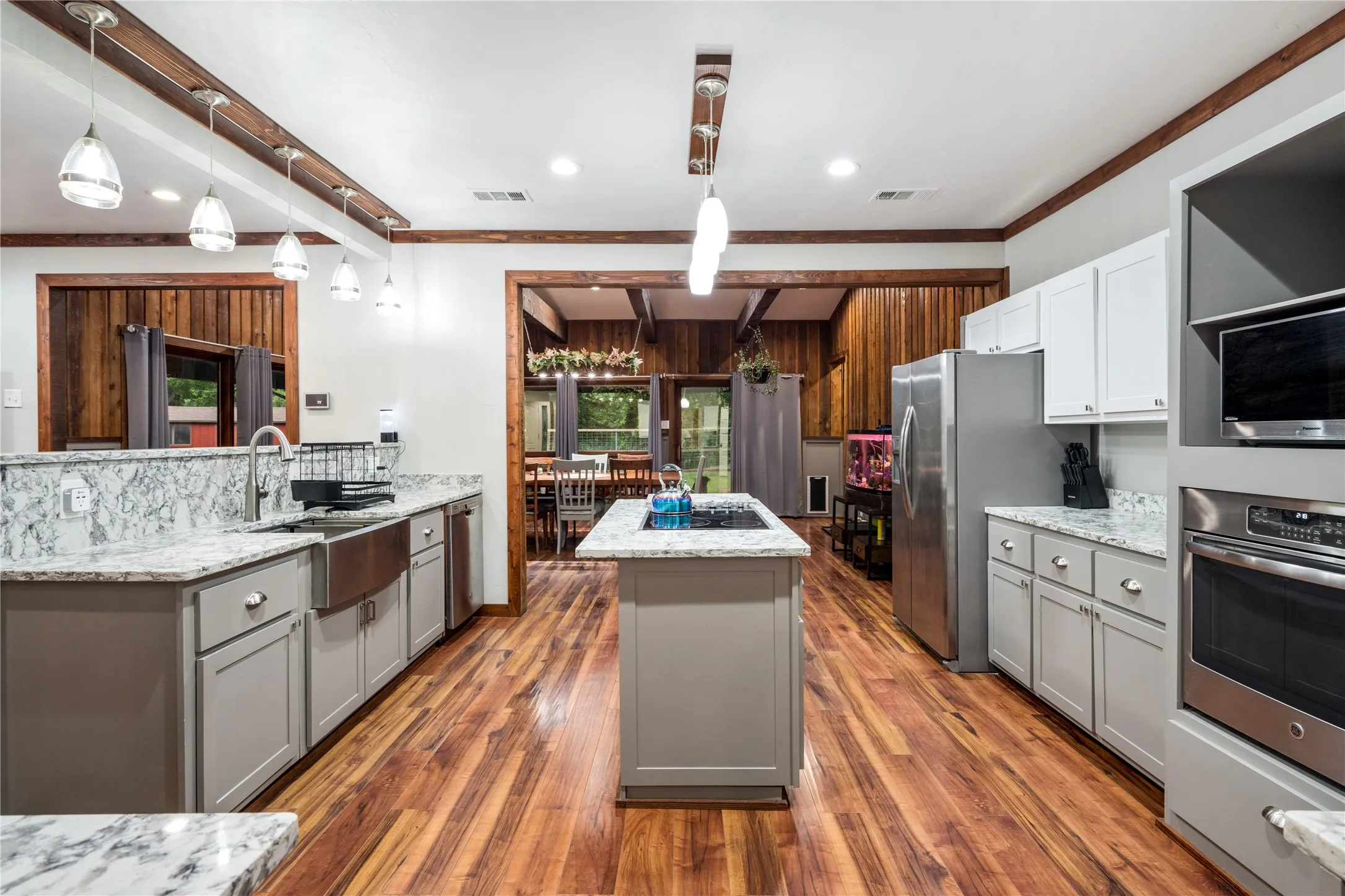 Kitchen with wood-finish flooring, light grey lower cabinetry, white upper cabinetry, and a center island with a built-in cooktop