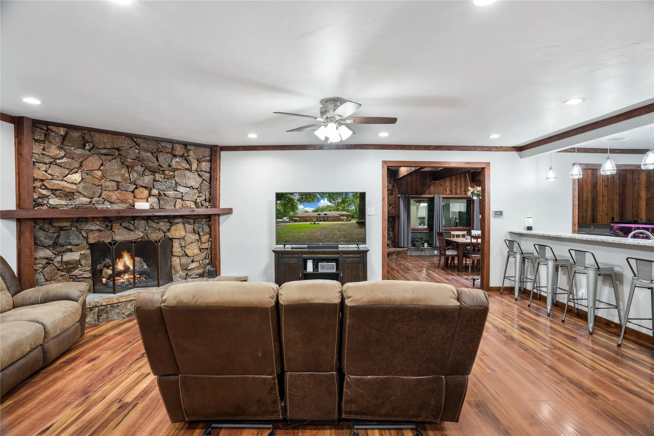 Spacious living area featuring a stone-faced fireplace with a wood mantel, wood-finish flooring, and a ceiling fan