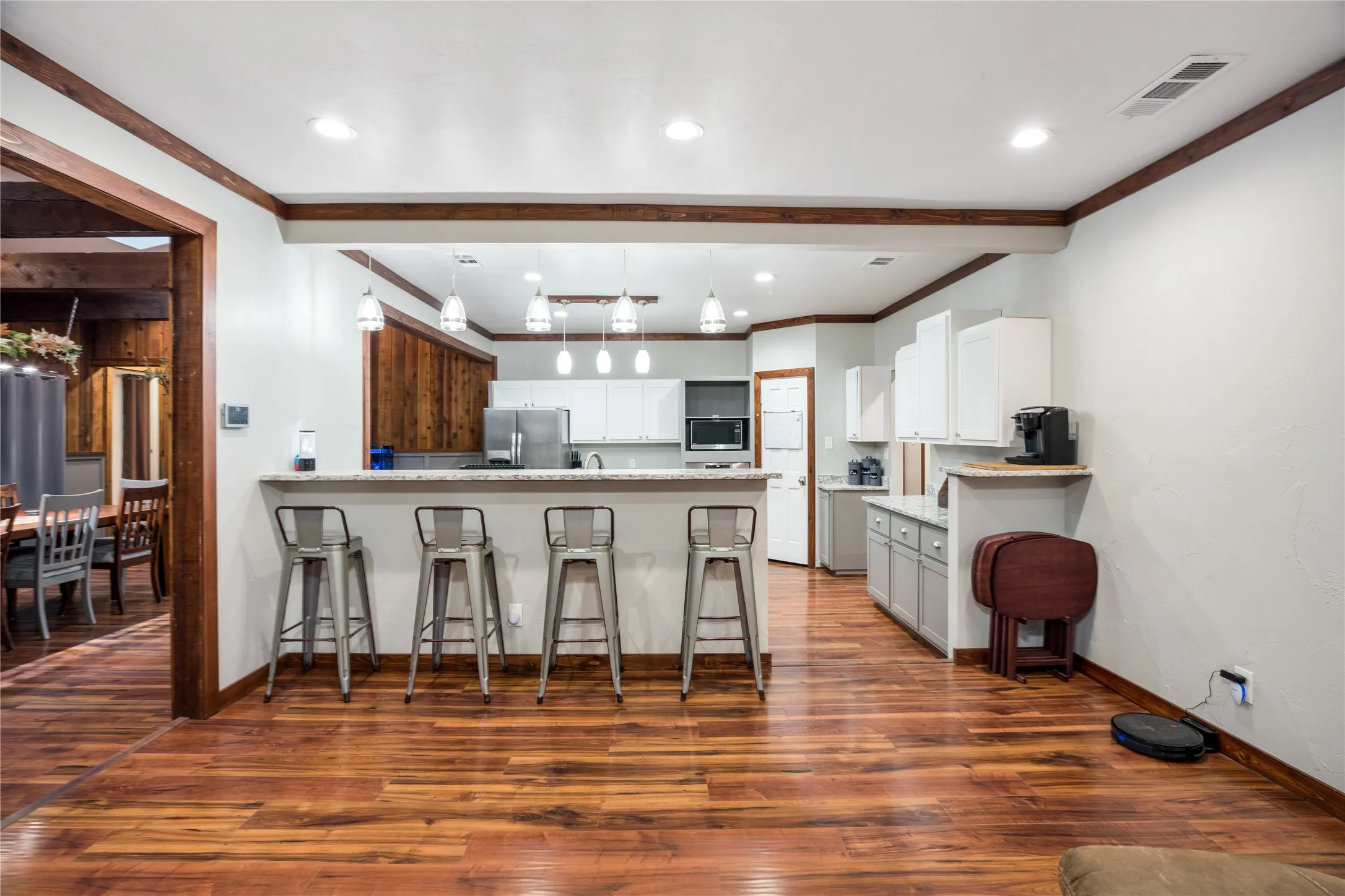 Open-concept kitchen featuring a breakfast bar with pendant lighting, wood-finish flooring, white cabinetry, stainless steel appliances, and wood trim accents