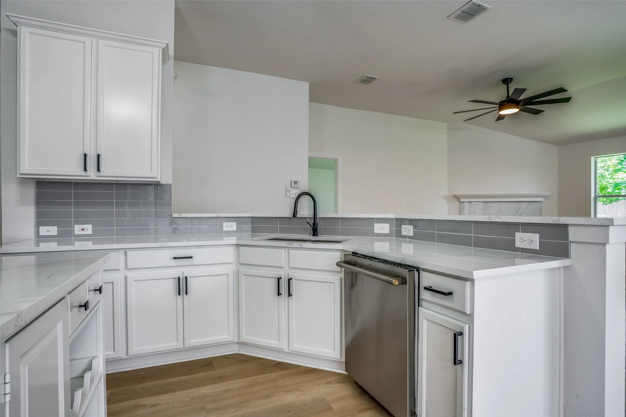 Kitchen featuring ceiling fan, light wood-type flooring, stainless steel dishwasher, and backsplash