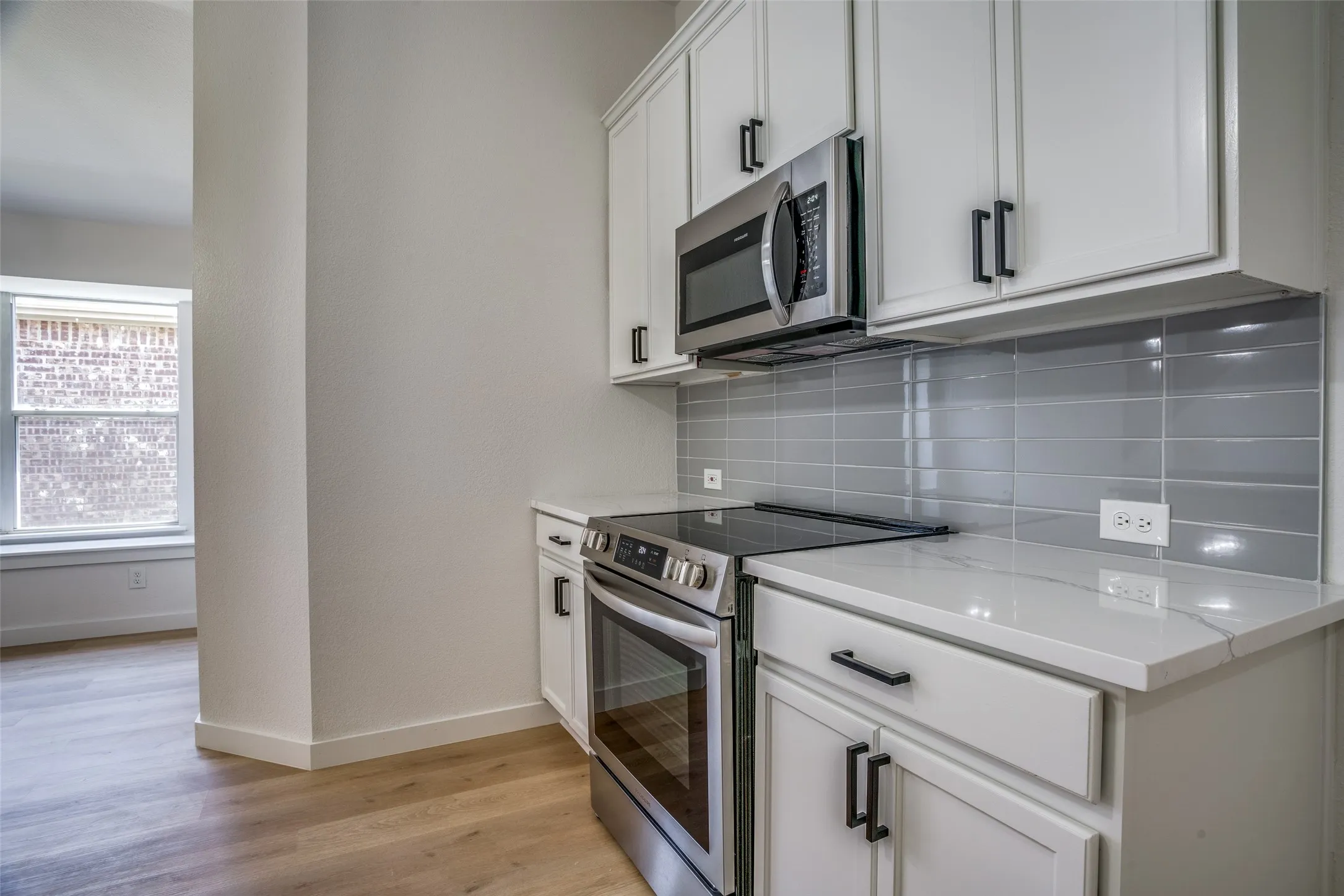 Kitchen featuring light wood-type flooring, light stone counters, backsplash, white cabinets, and appliances with stainless steel finishes