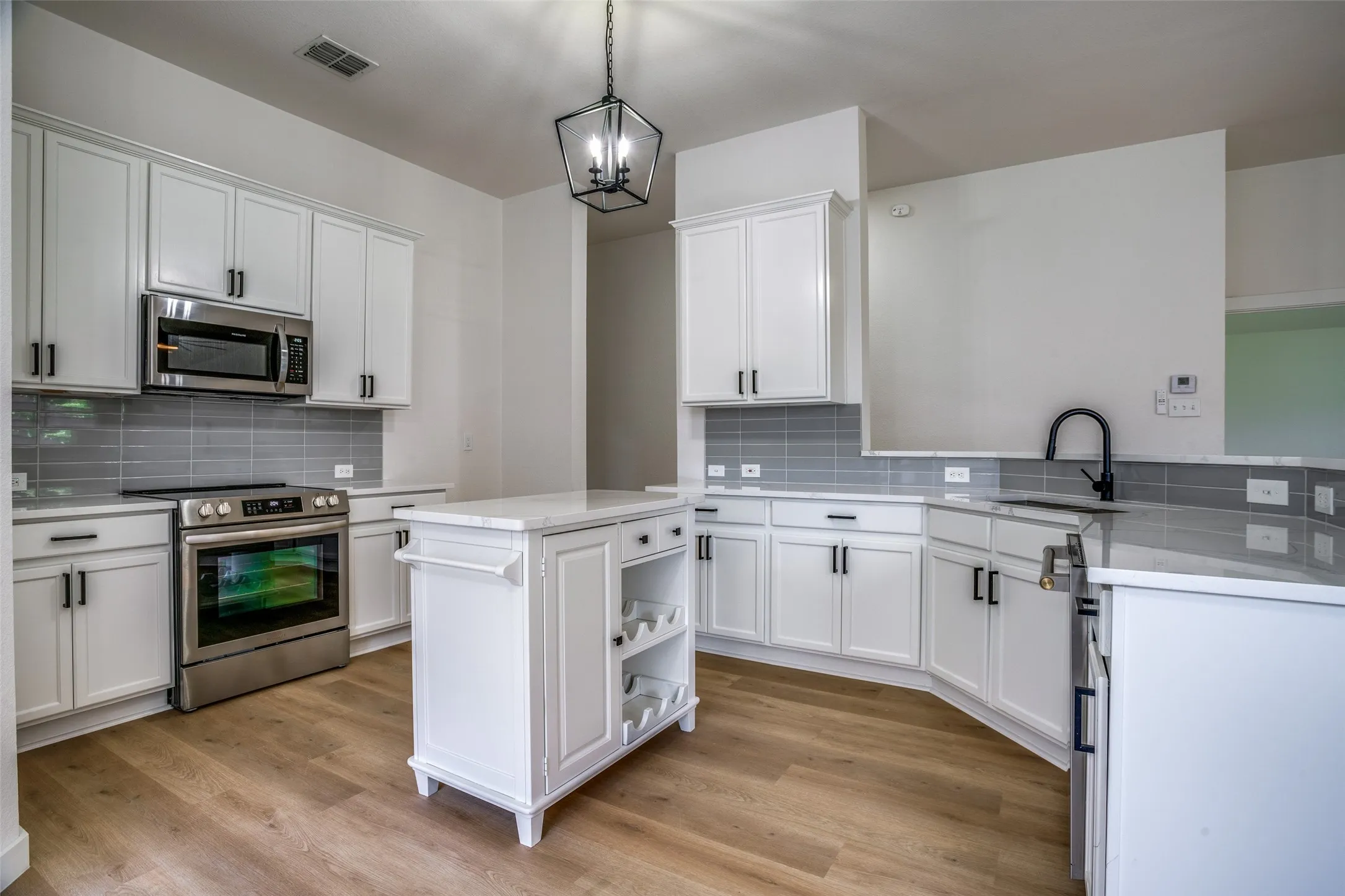 Kitchen featuring decorative light fixtures, white cabinetry, light wood-type flooring, and stainless steel appliances