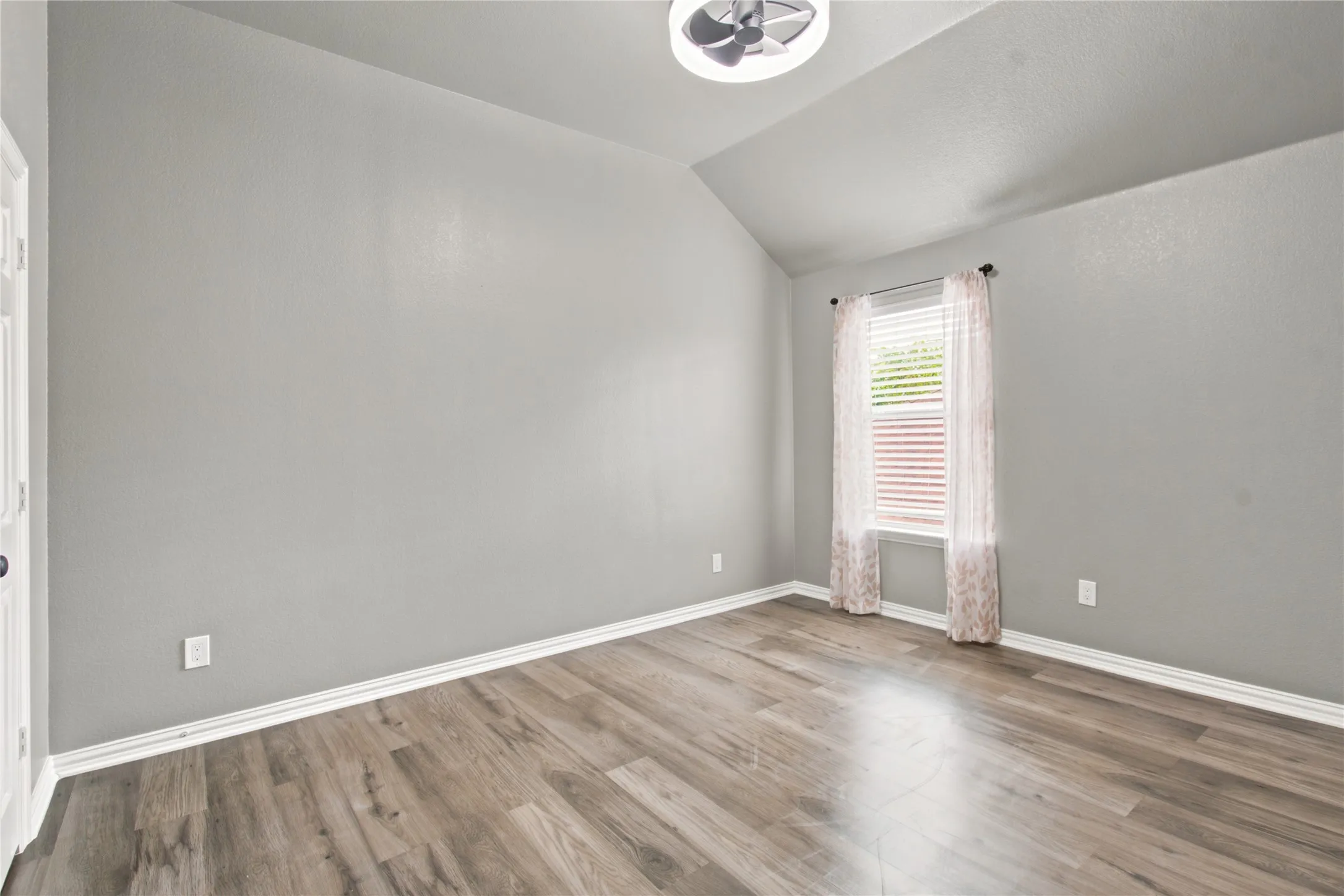 Vaulted ceiling room featuring wood-finish flooring, a window with horizontal blinds, and a contemporary ceiling fan