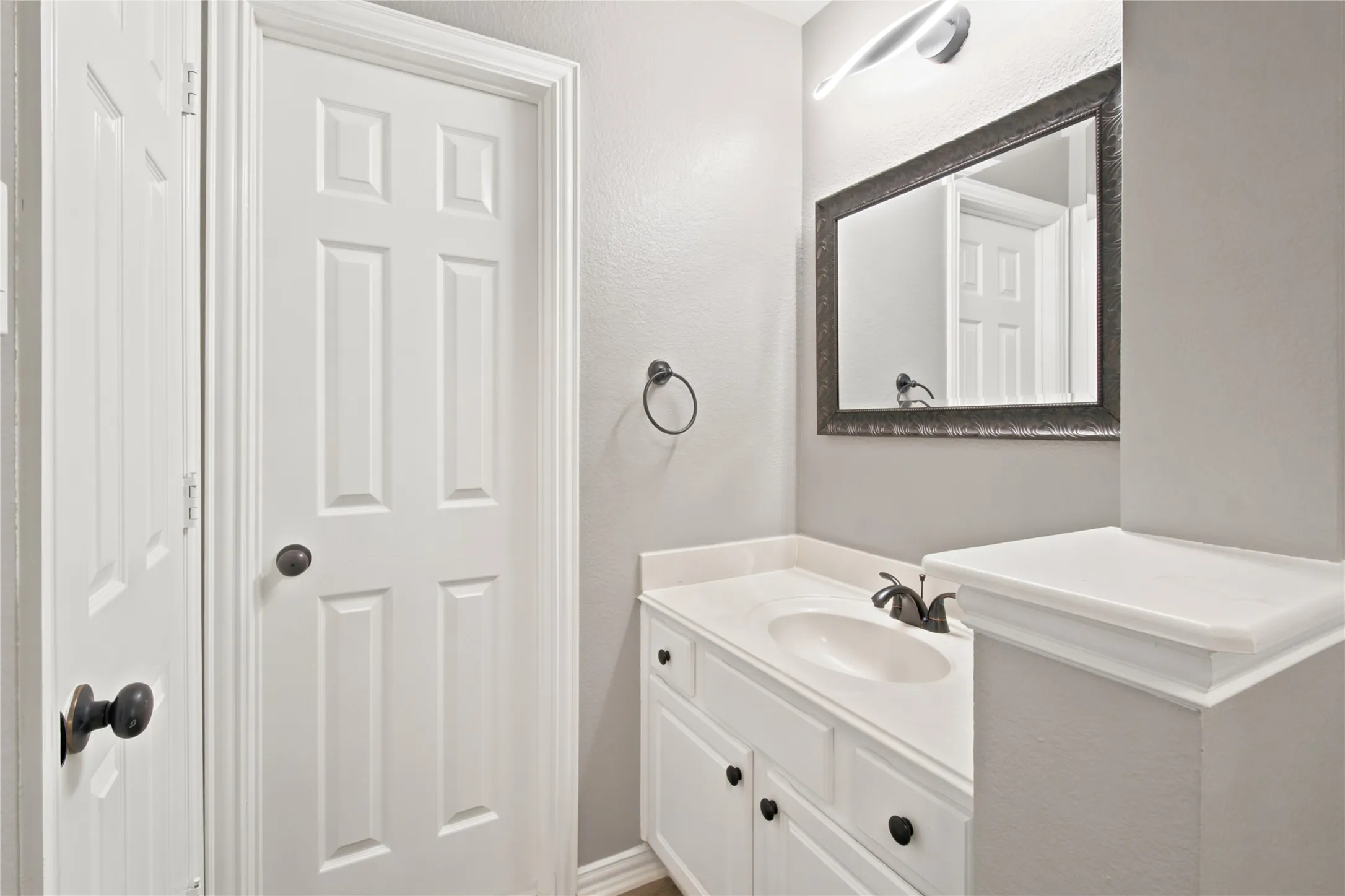 Bathroom vanity with white cabinetry, a single basin sink, and a countertop featuring an integrated backsplash
