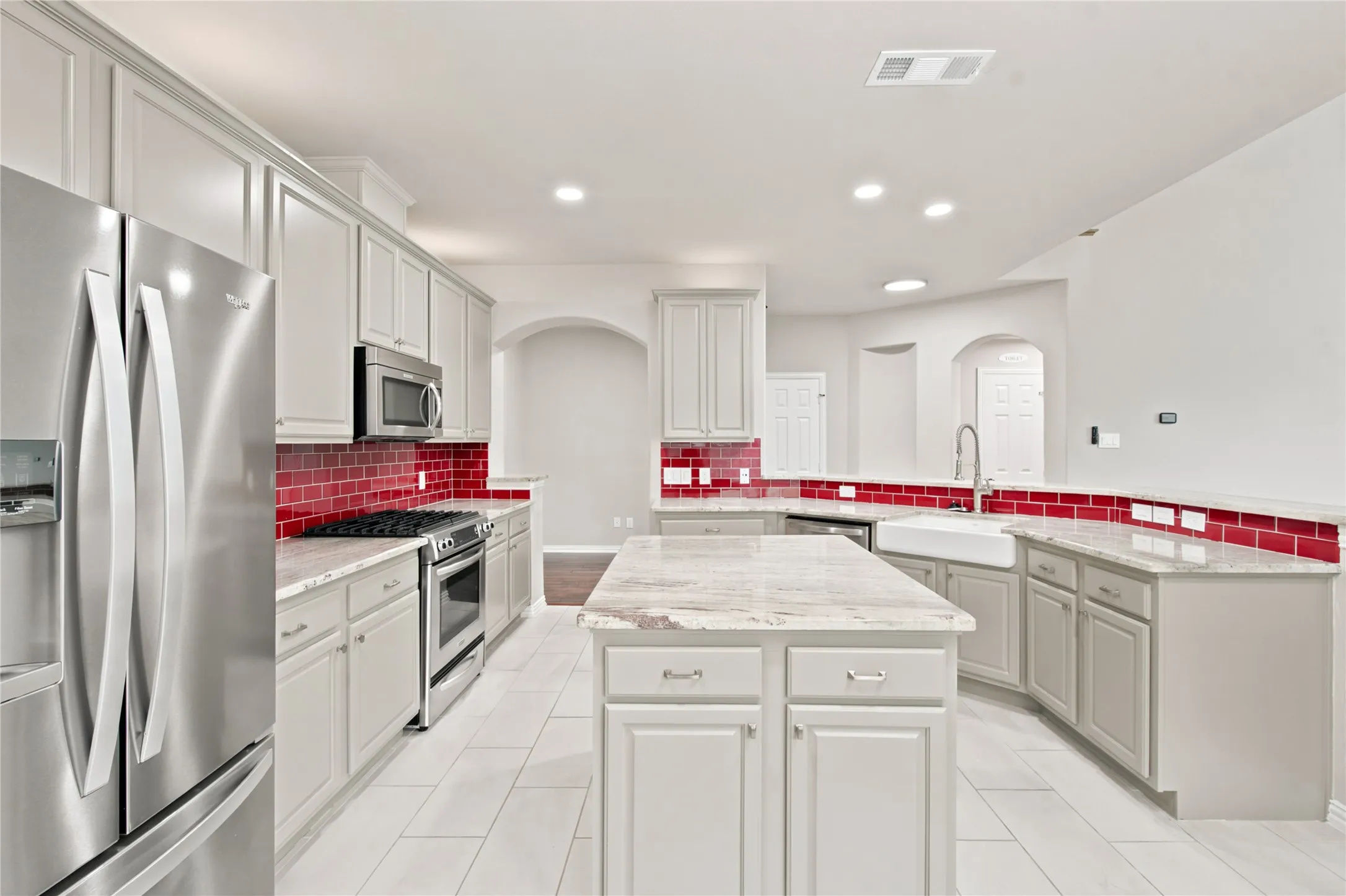 Kitchen featuring a central island, light-toned cabinetry, stainless steel appliances, a farmhouse-style sink, and a red tile backsplash
