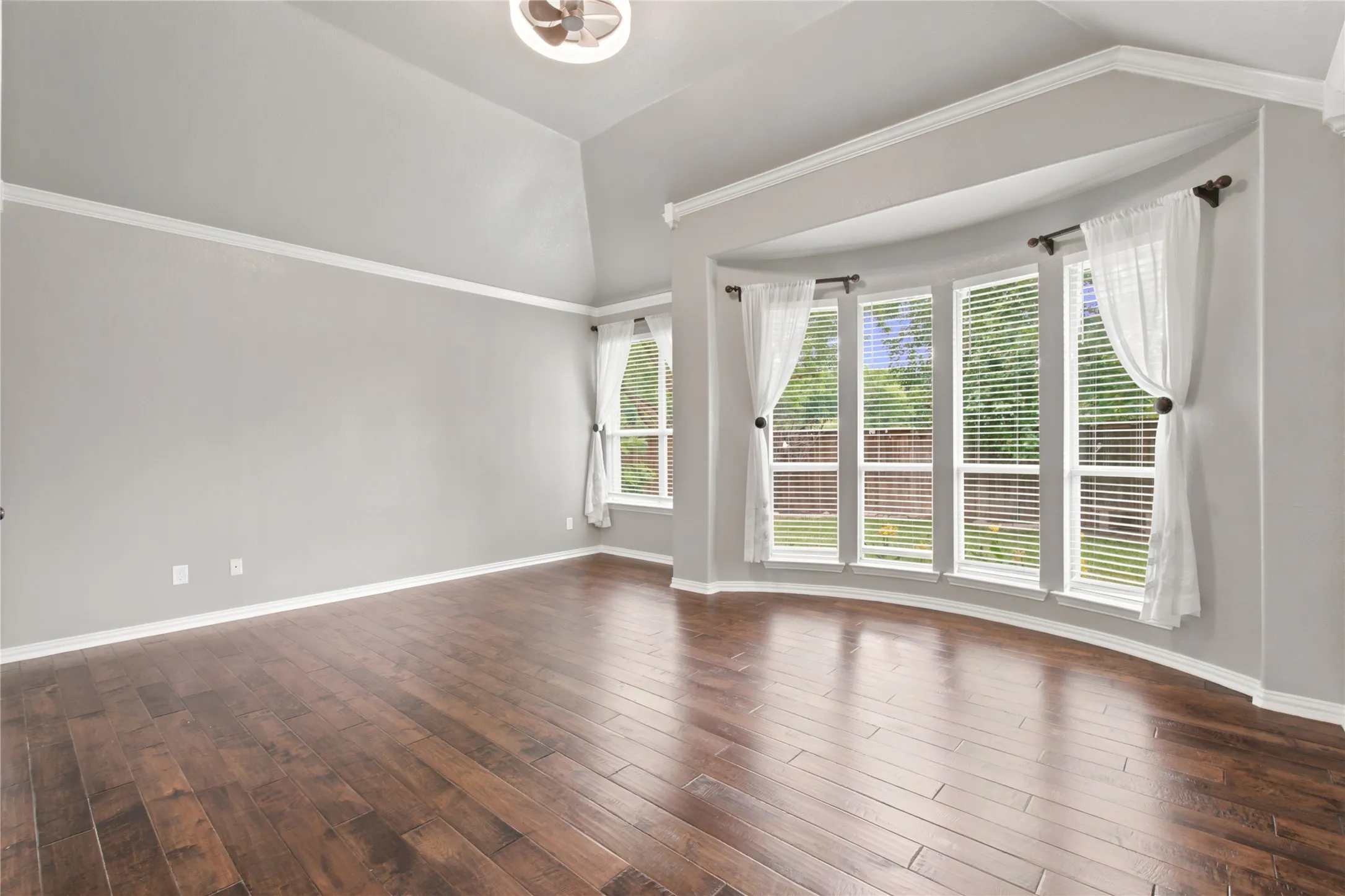Curved bay window with four individual windows, showcasing wood-finish flooring, vaulted ceilings, crown molding, and a modern ceiling fan