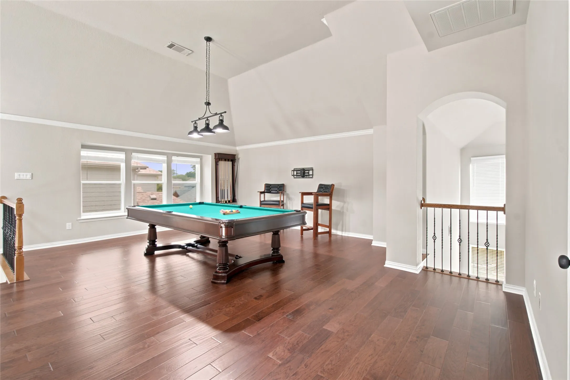 Spacious open area featuring high vaulted ceilings, multiple windows with blinds, dark wood-finish flooring, and an arched entryway