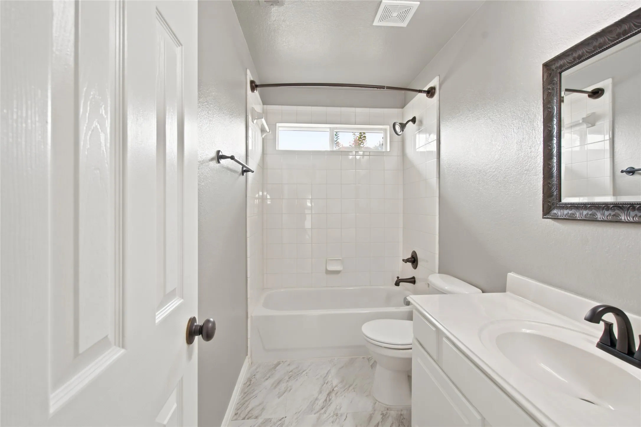 Bathroom featuring a white bathtub with subway tile surround and dark bronze fixtures, a white vanity with a single basin sink, and a framed mirror