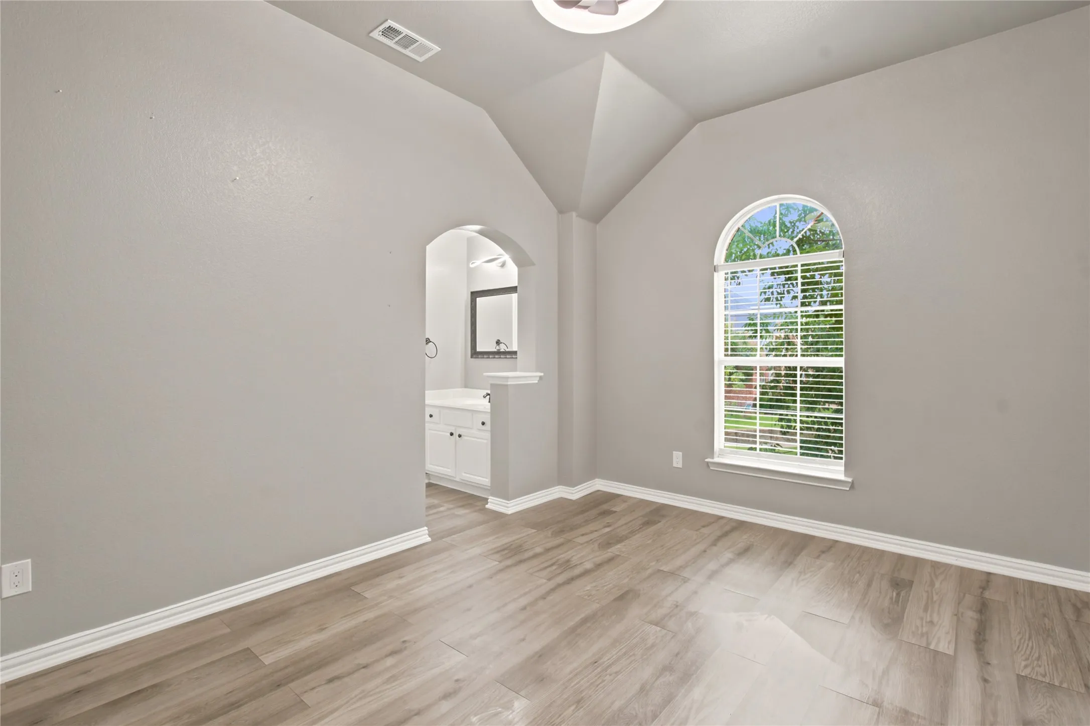 Vaulted ceiling room featuring wood-finish flooring and a prominent arched window with blinds