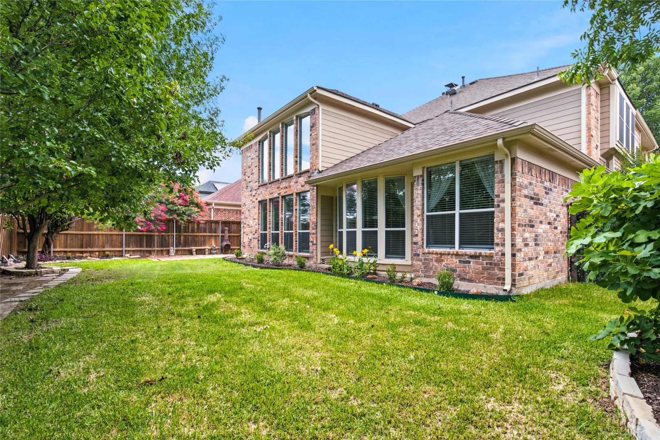 Expansive backyard featuring a manicured lawn, full privacy fencing, and mature trees