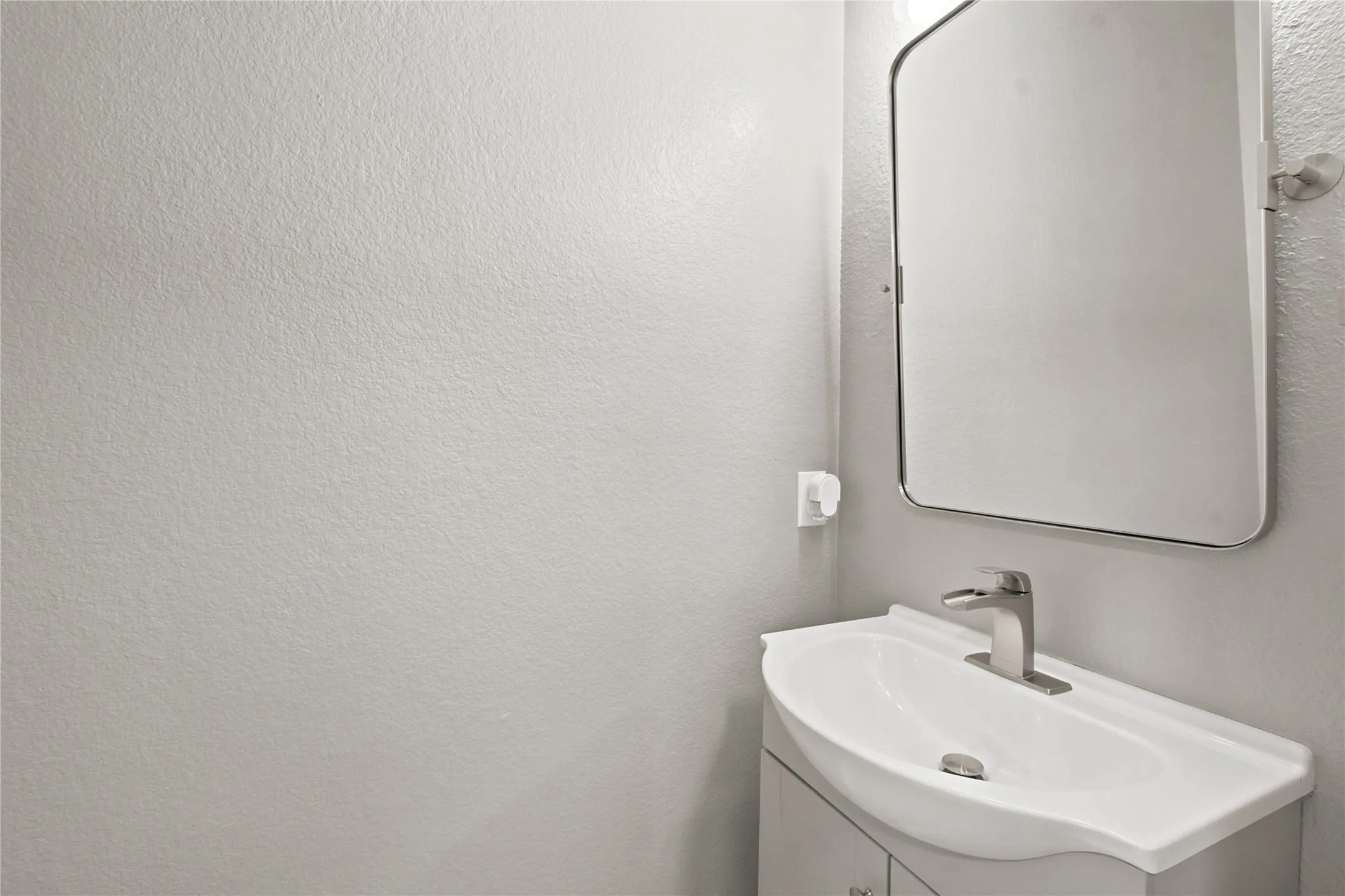 White vanity with an integrated sink and a single-handle faucet, complemented by a rectangular frameless mirror