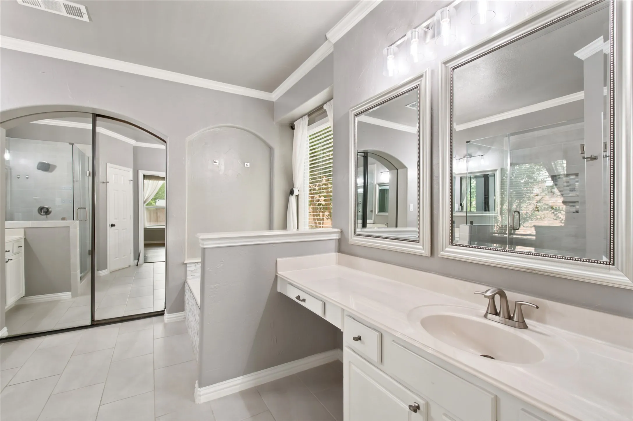 Bathroom vanity featuring dual framed mirrors, a single undermount sink with a brushed nickel faucet, and a spacious countertop with an integrated dressing area