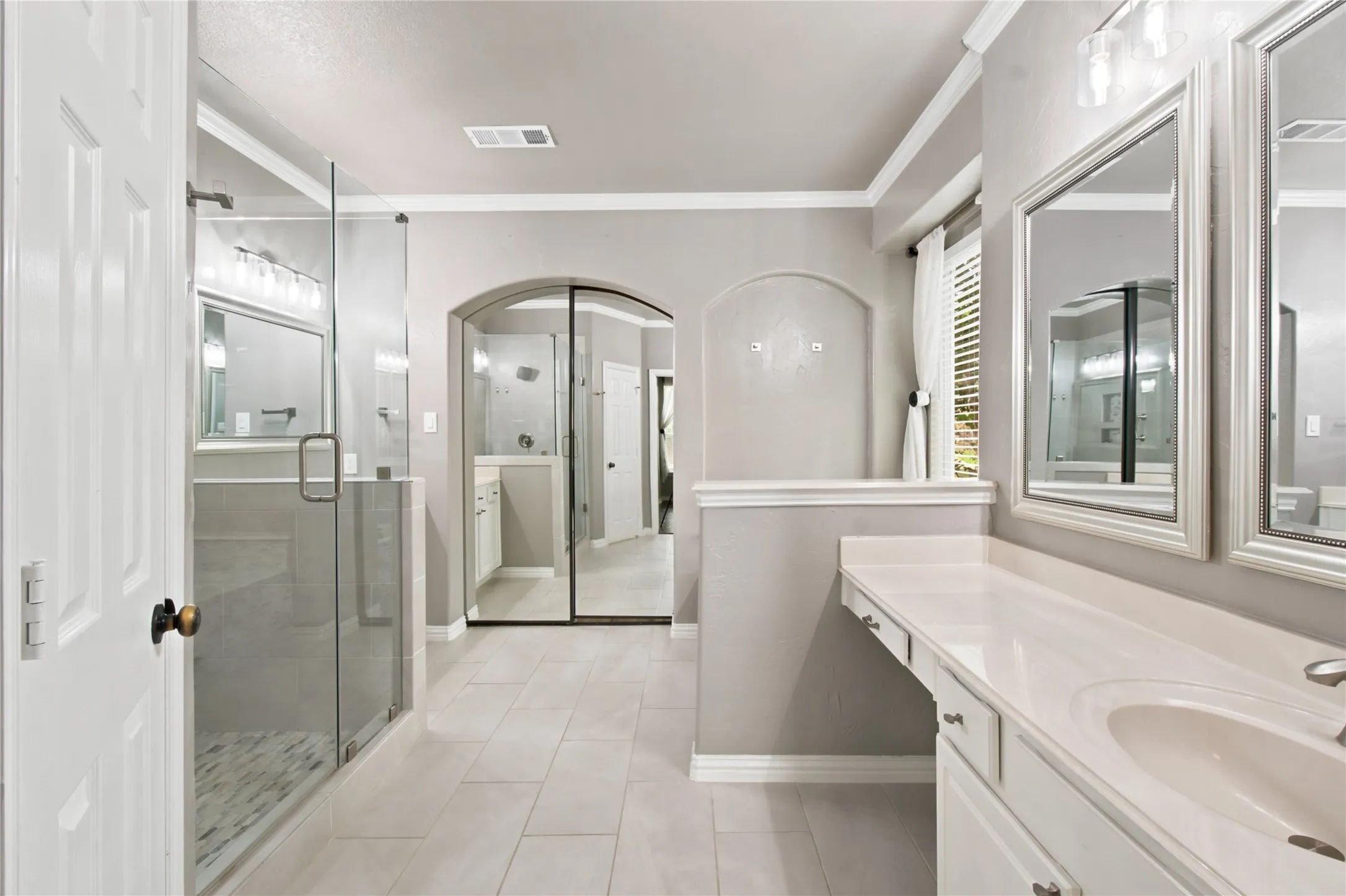 Bathroom featuring a glass-enclosed shower with tile flooring, dual vanity with undermount sinks and light-toned countertops, decorative framed mirrors, and archway architectural details