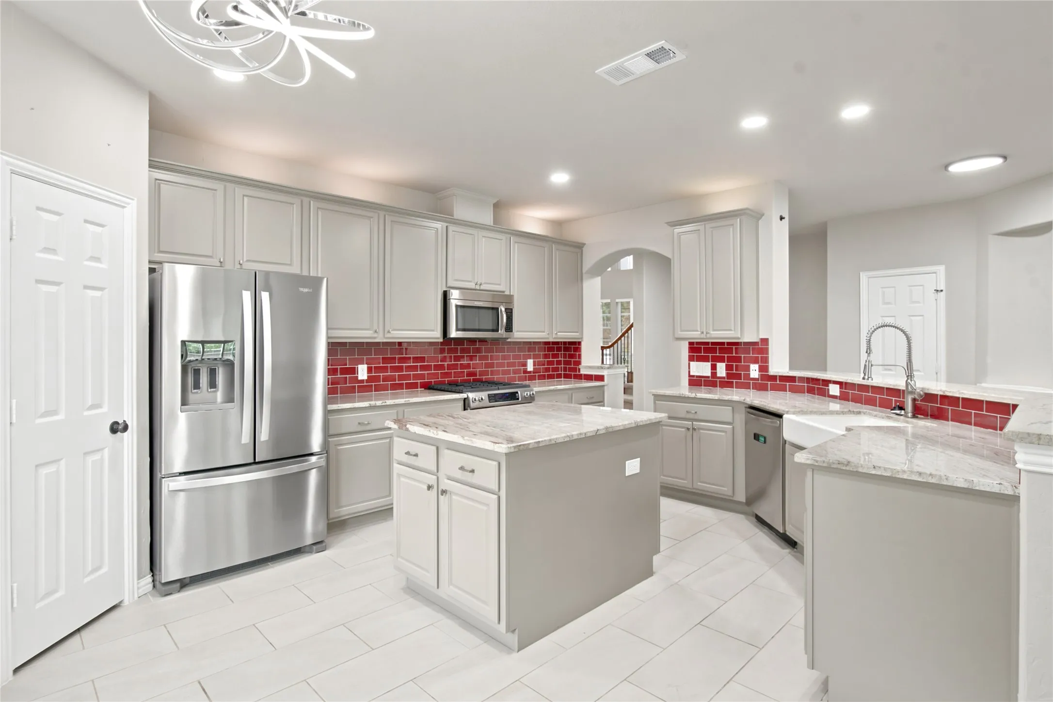Kitchen featuring light gray cabinetry, red subway tile backsplash, stainless steel appliances, a center island, and light-toned flooring