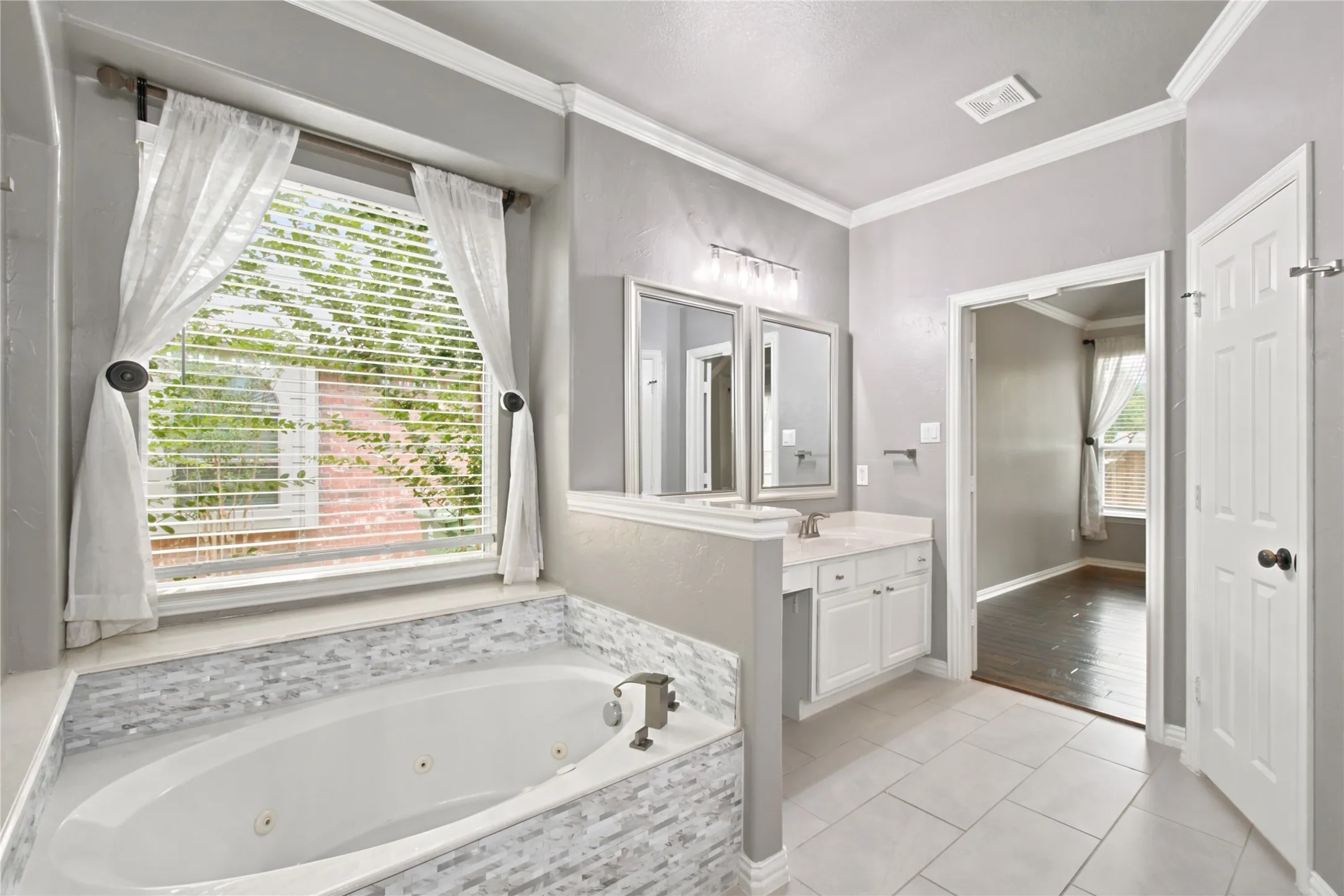 Bathroom featuring a built-in jetted tub with mosaic tile surround, dual vanity with white cabinetry and framed mirrors, and light gray wall paint