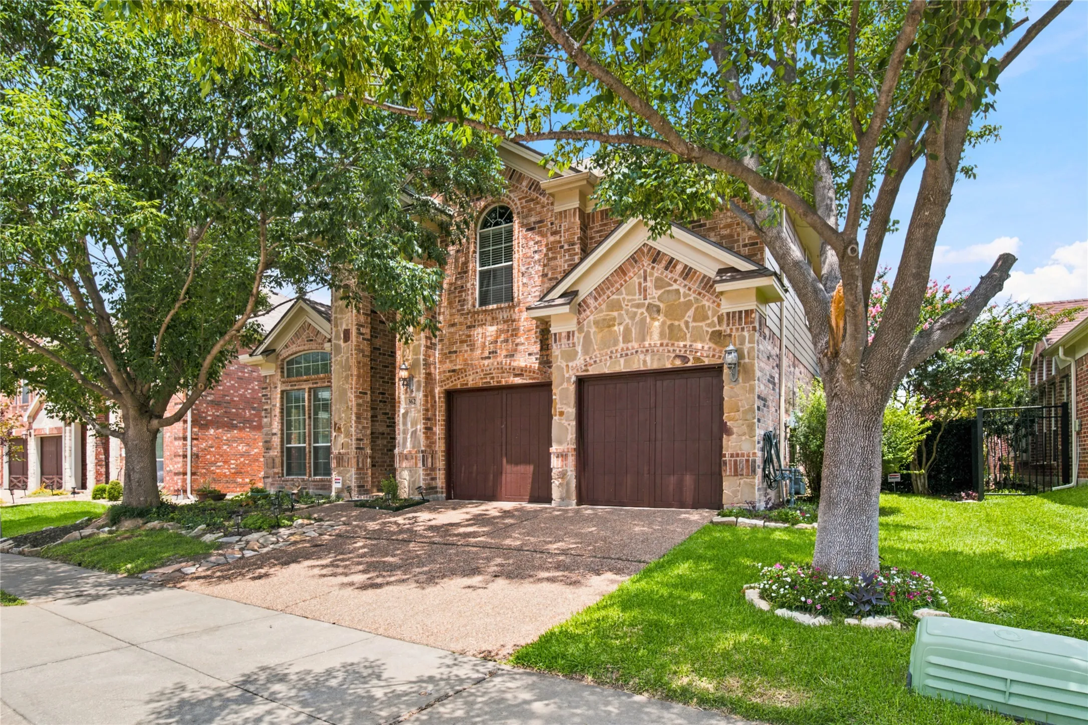 Two-story brick and stone facade residence featuring arched windows, a two-car garage with wood-finish doors, and a concrete sidewalk