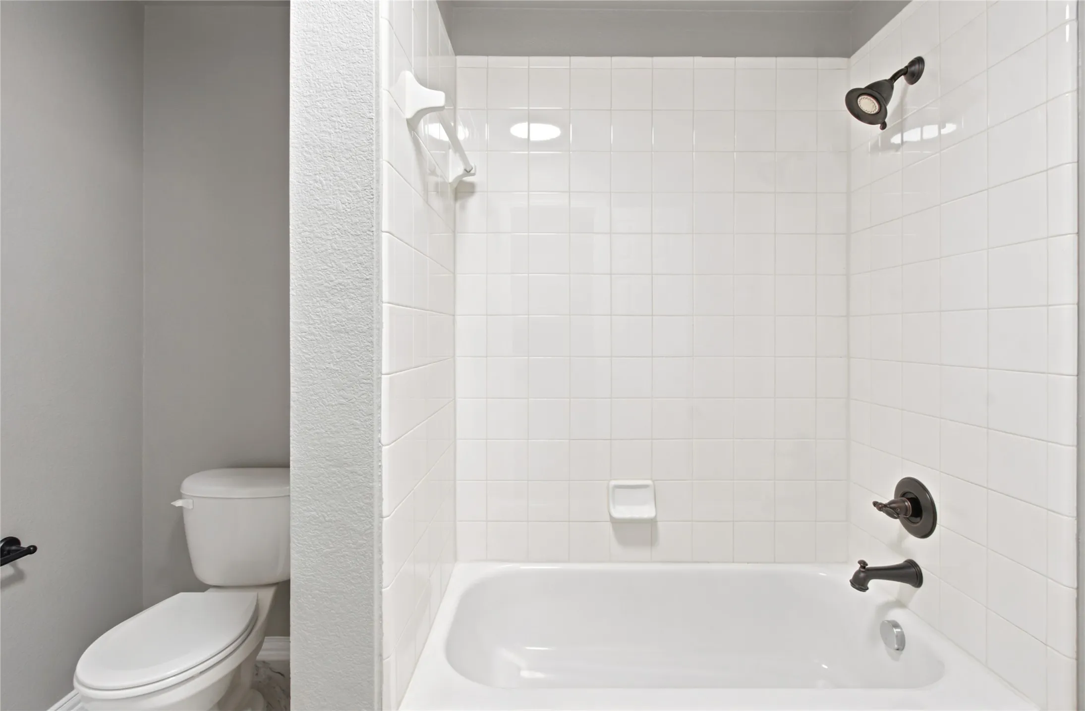 White tiled tub and shower combination with dark bronze fixtures