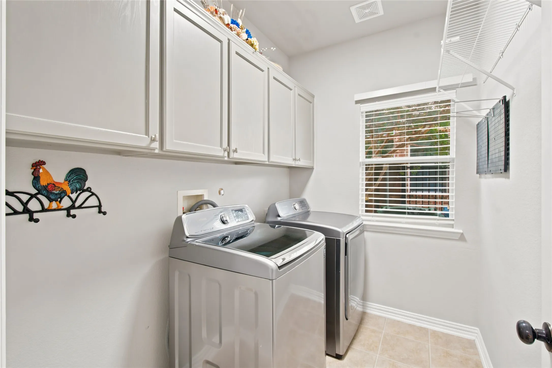 Dedicated utility room featuring light-colored cabinetry, a single window with blinds, and tile flooring