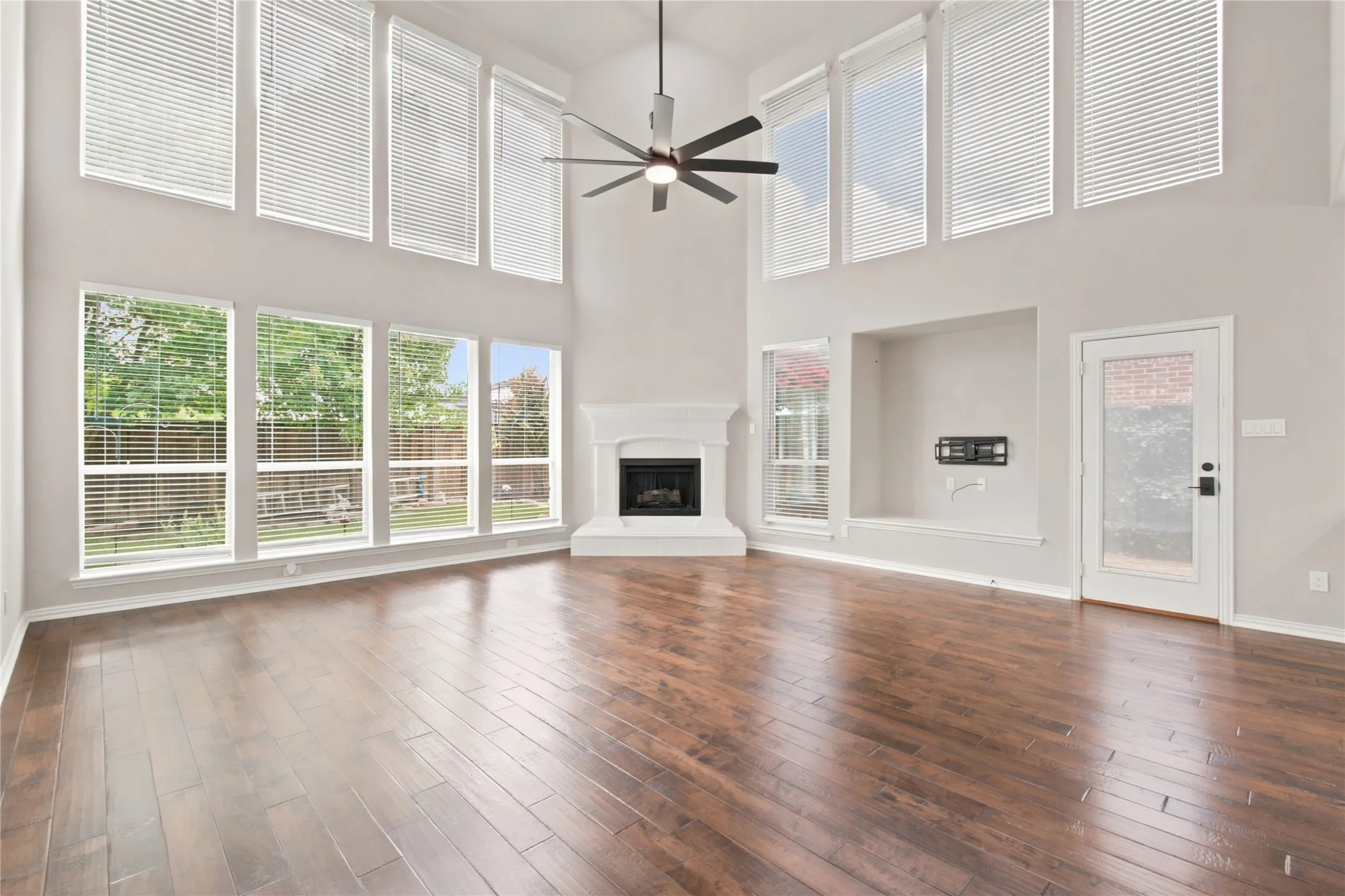 Spacious living area featuring high ceilings, wood-finish flooring, and a fireplace with a white mantel