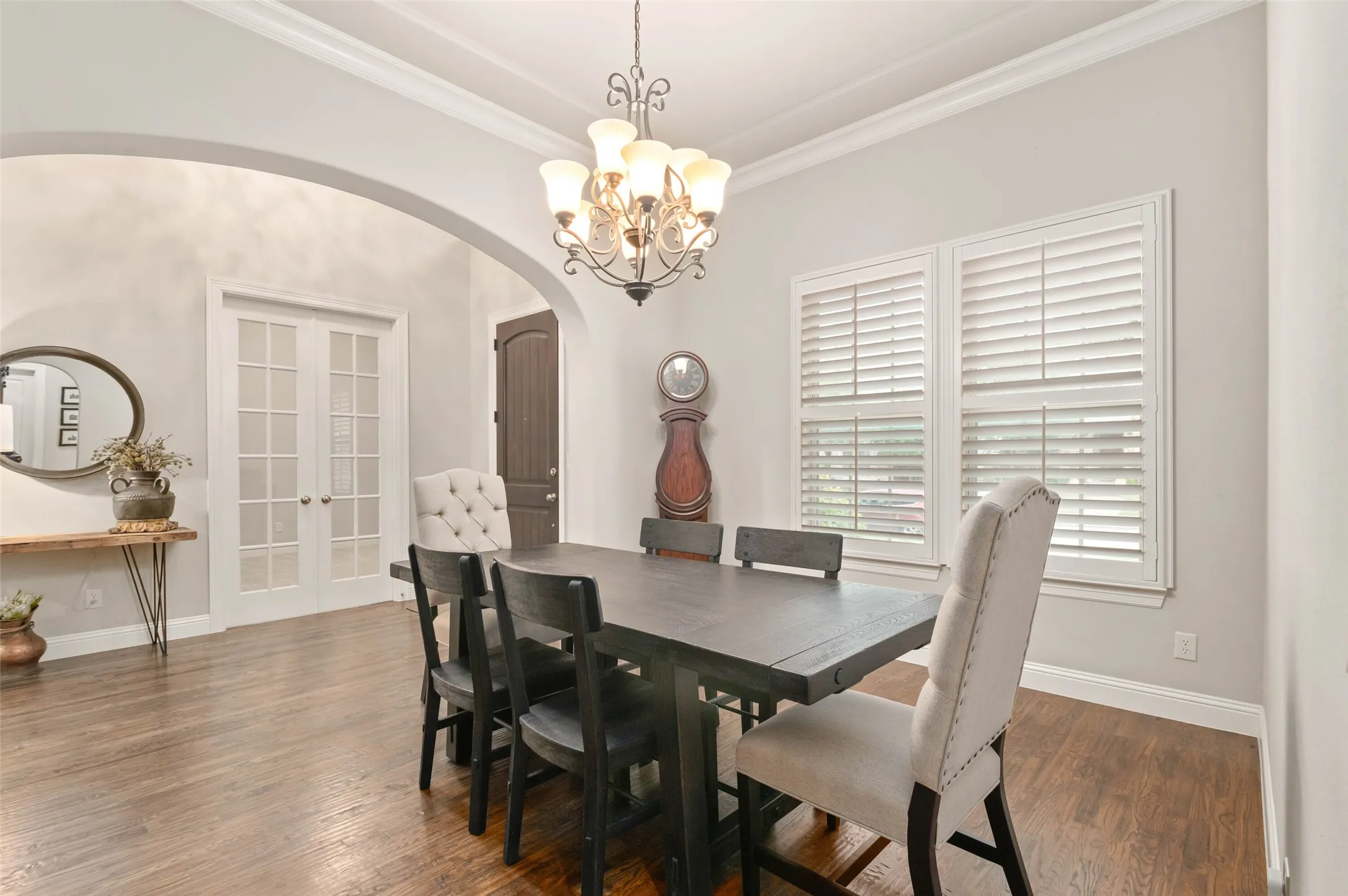 Virtually staged formal dining space featuring wood-finish flooring, an arched entryway, double French doors, and two windows with white plantation shutters