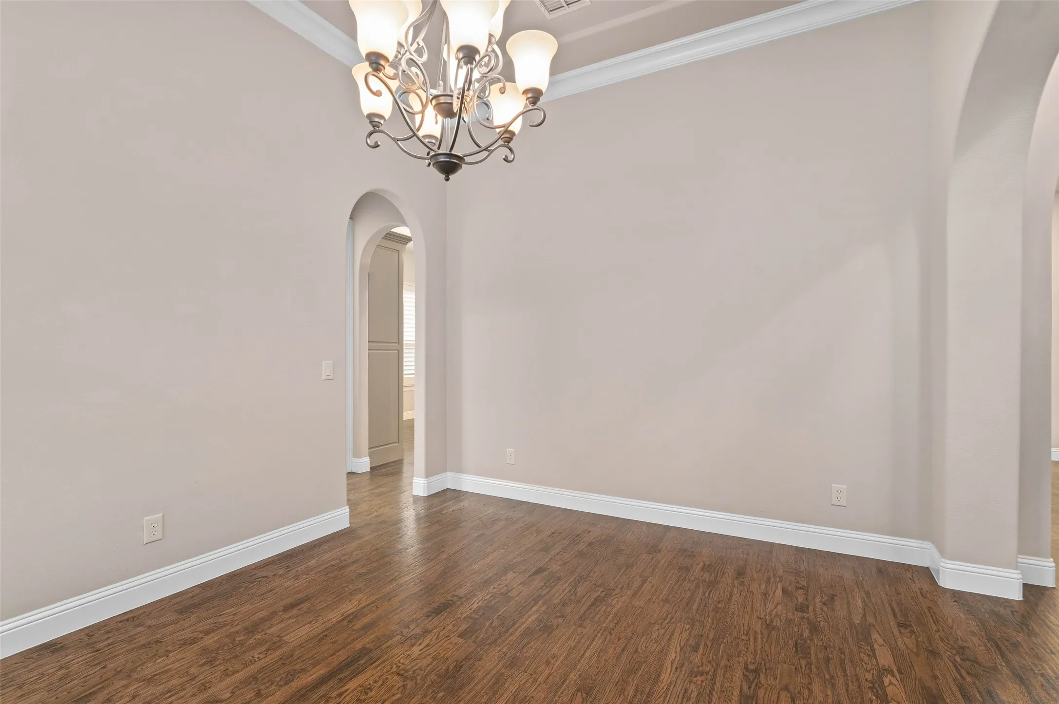 Formal dining space featuring wood-finish flooring, an arched entryway, double French doors, and two windows with white plantation shutters