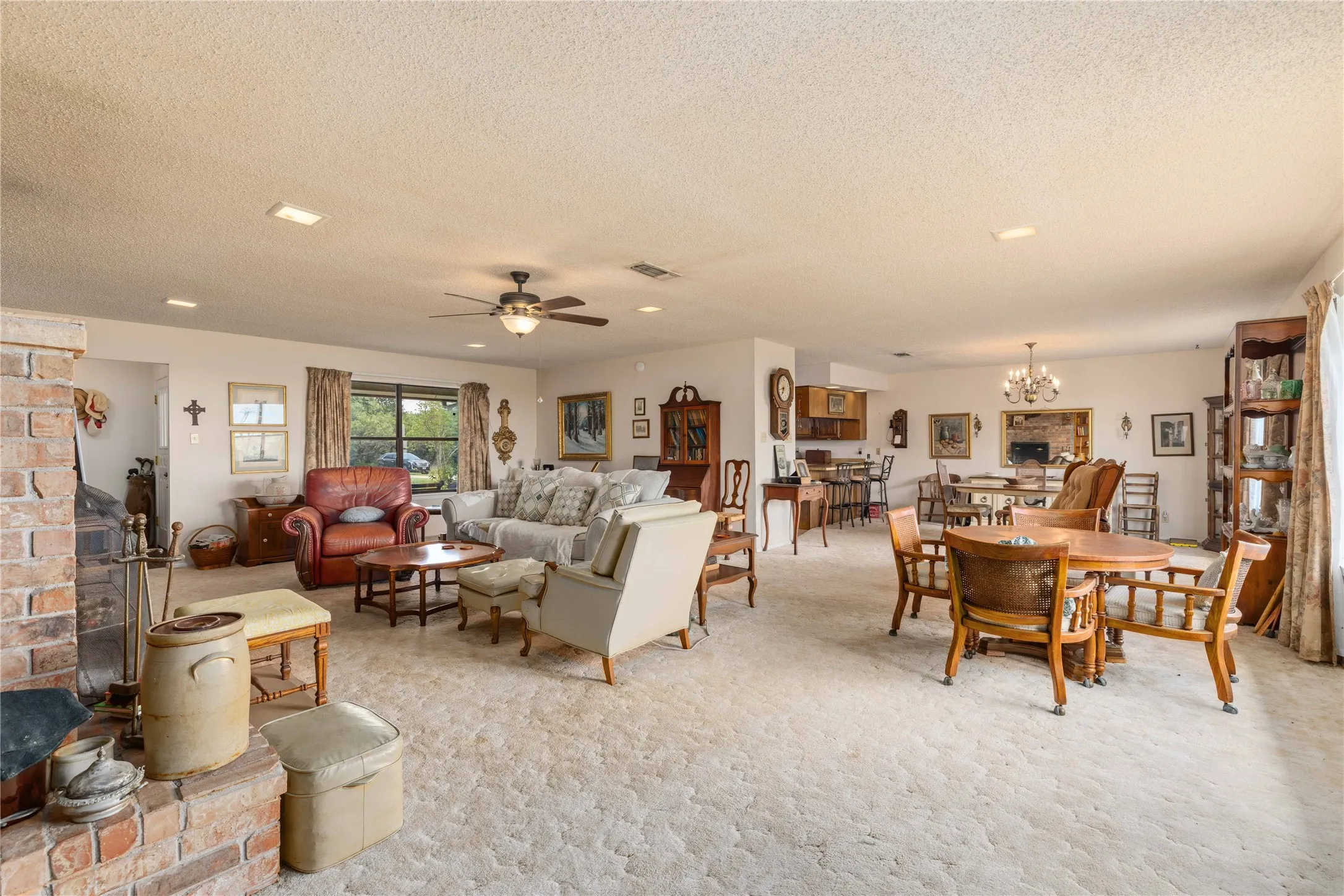 Spacious open-concept living area featuring a brick fireplace, ceiling fan, recessed lighting, and large windows