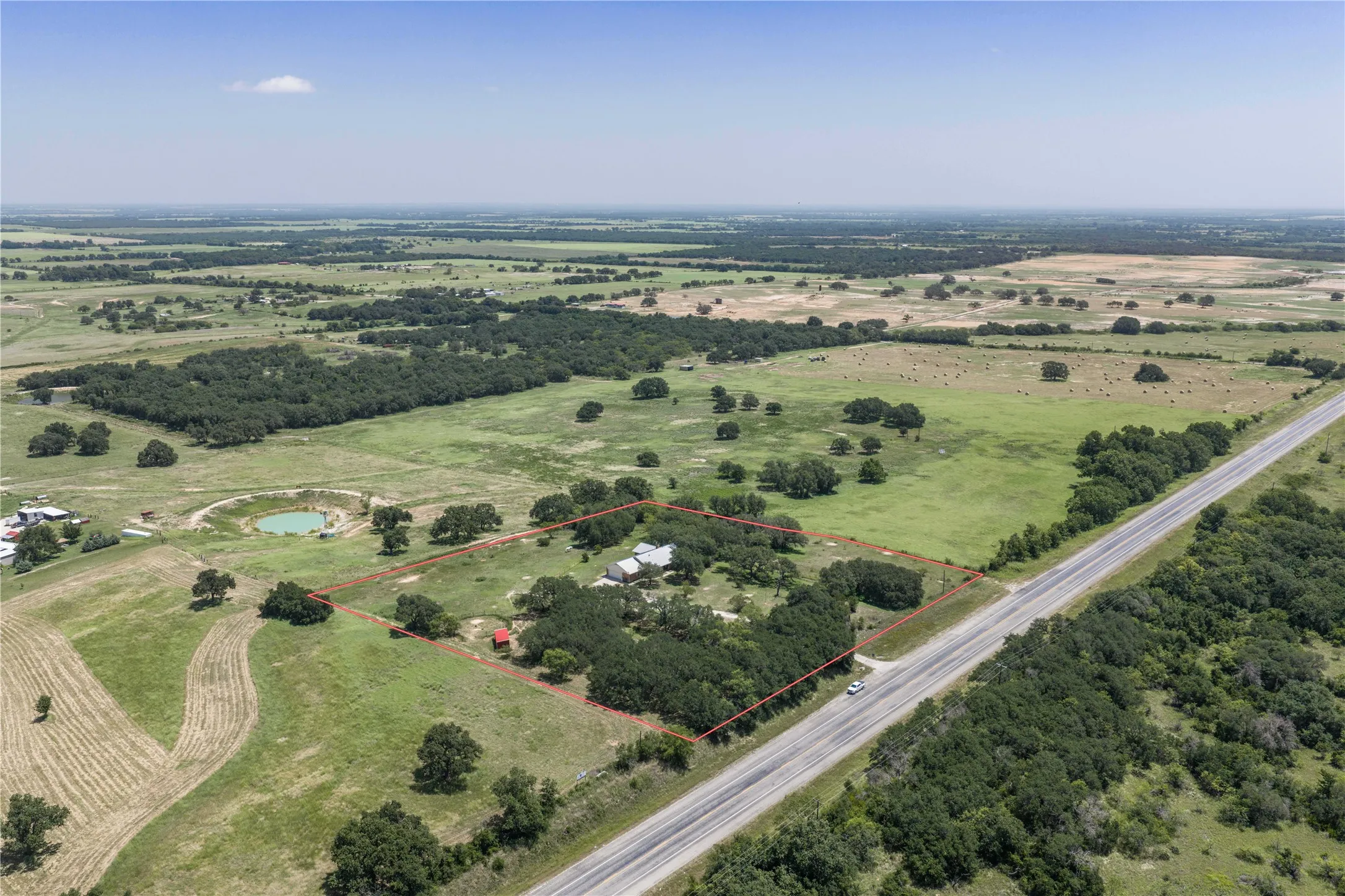 Expansive rural property featuring a prominent main residence, multiple outbuildings, mature trees, a private pond, and direct road frontage