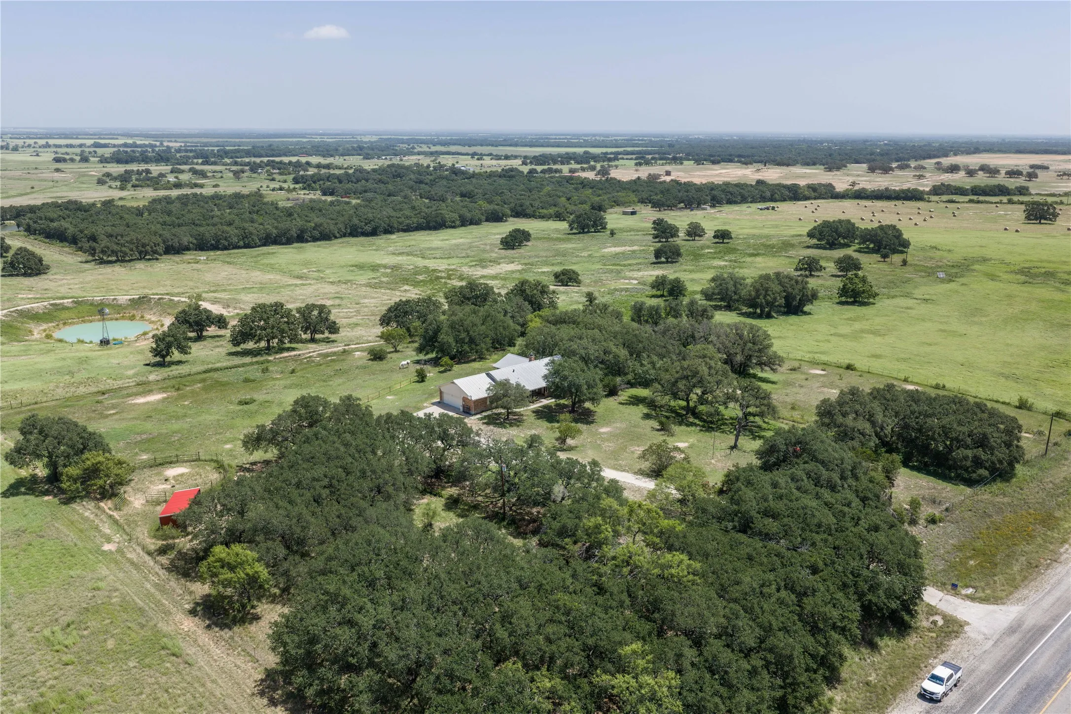 Expansive rural property featuring a single-story residence, mature tree coverage, a pond with a windmill, and a red outbuilding