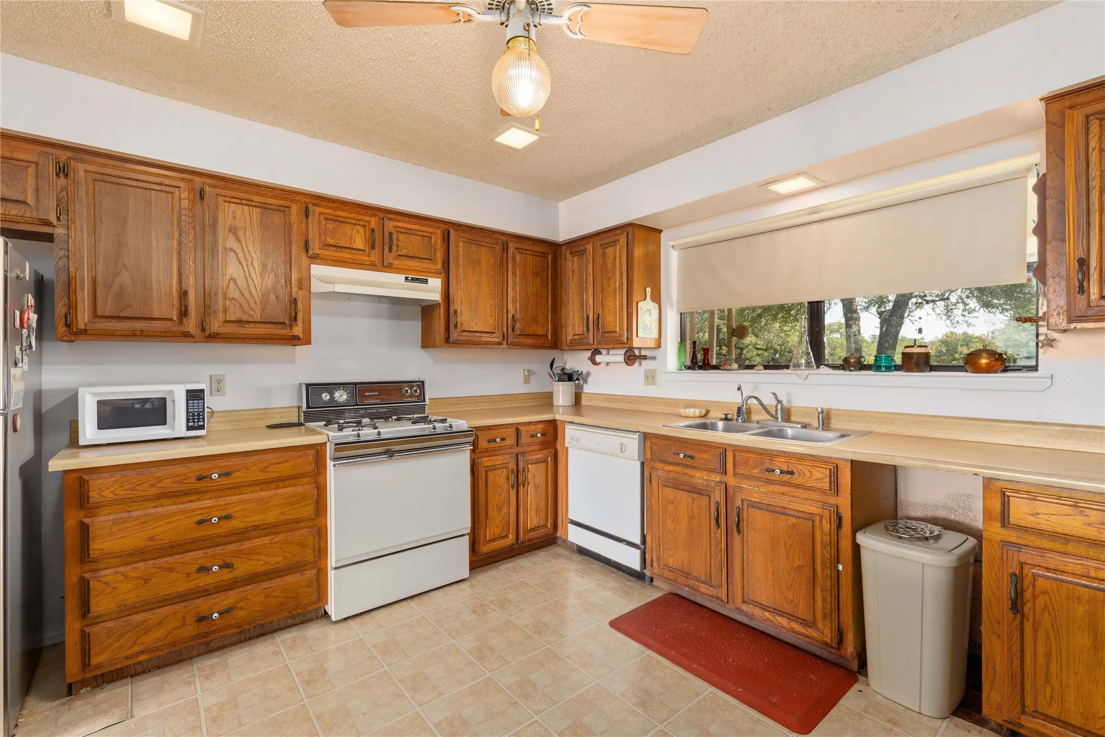 Kitchen featuring wood cabinetry, laminate countertops, a gas range, a double basin sink, and tile flooring