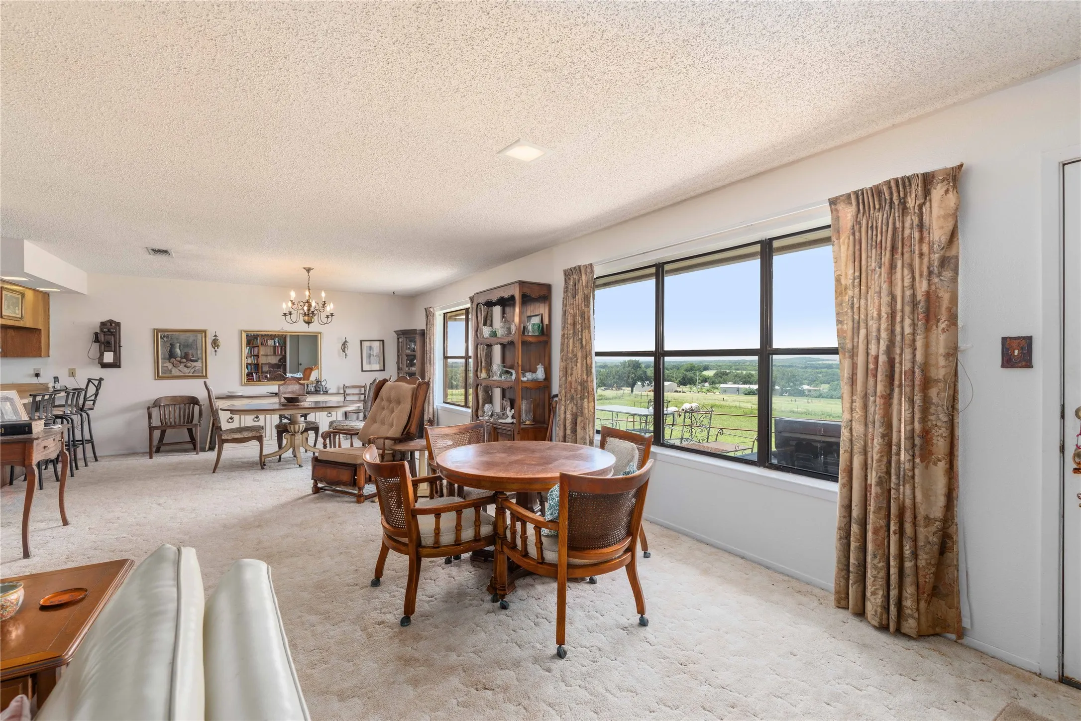 Expansive interior space featuring a large window with distant outdoor scenery, carpeted flooring, a chandelier fixture, and recessed lighting