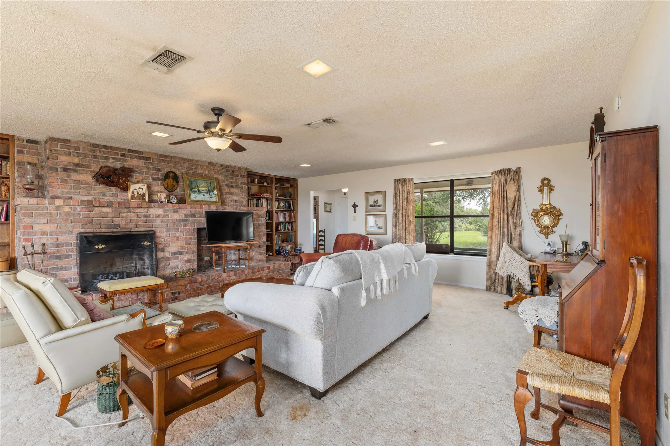 Spacious living area featuring a brick fireplace, built-in shelving, ceiling fan, recessed lighting, and large windows
