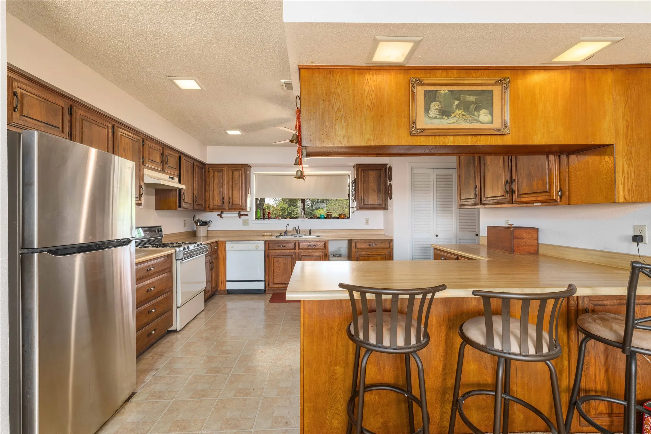 Kitchen featuring wood cabinetry, stainless steel refrigerator, white appliances, a breakfast bar, and tile flooring