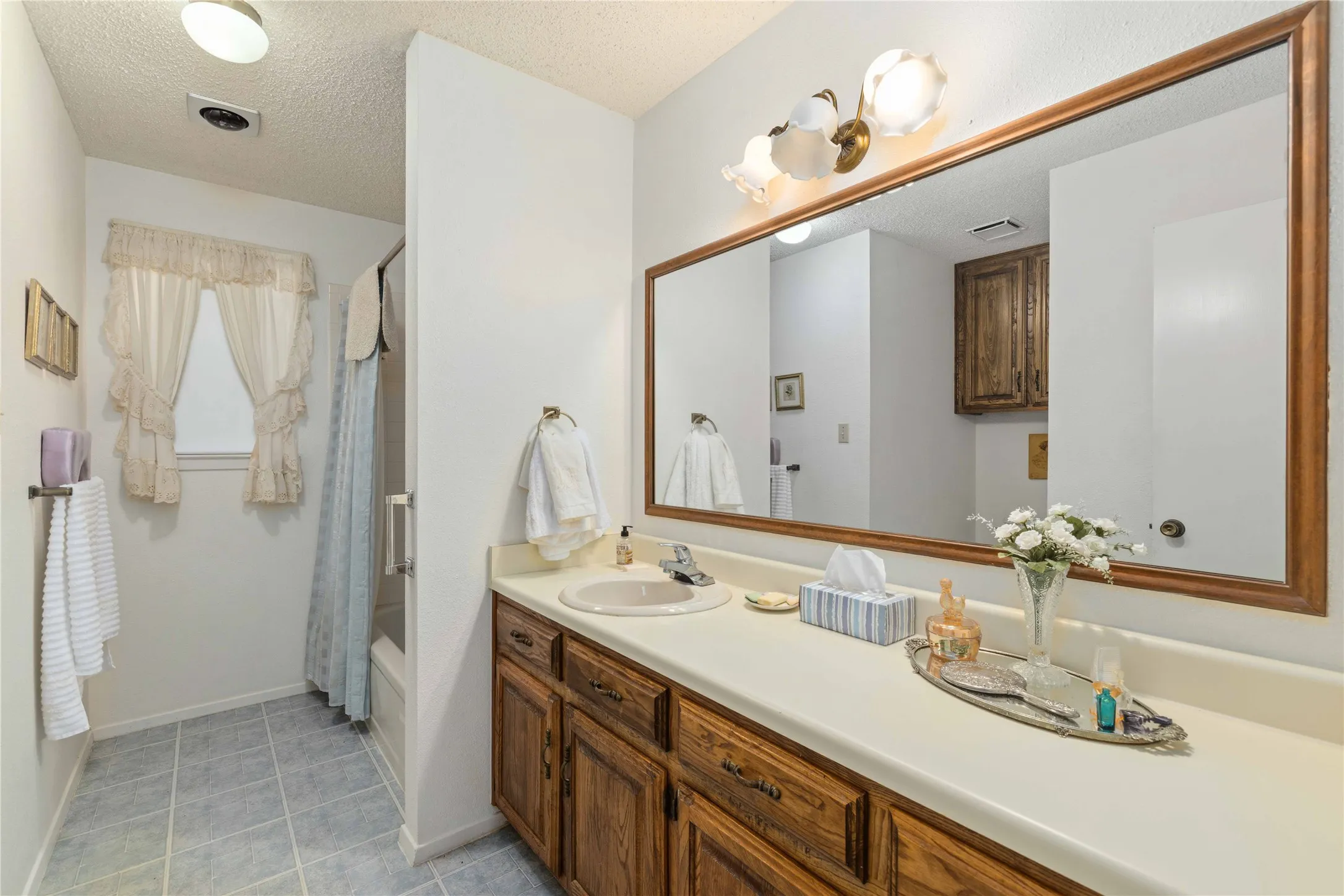 Bathroom vanity featuring a light-colored countertop, wood-finish cabinetry, and a full-width framed mirror