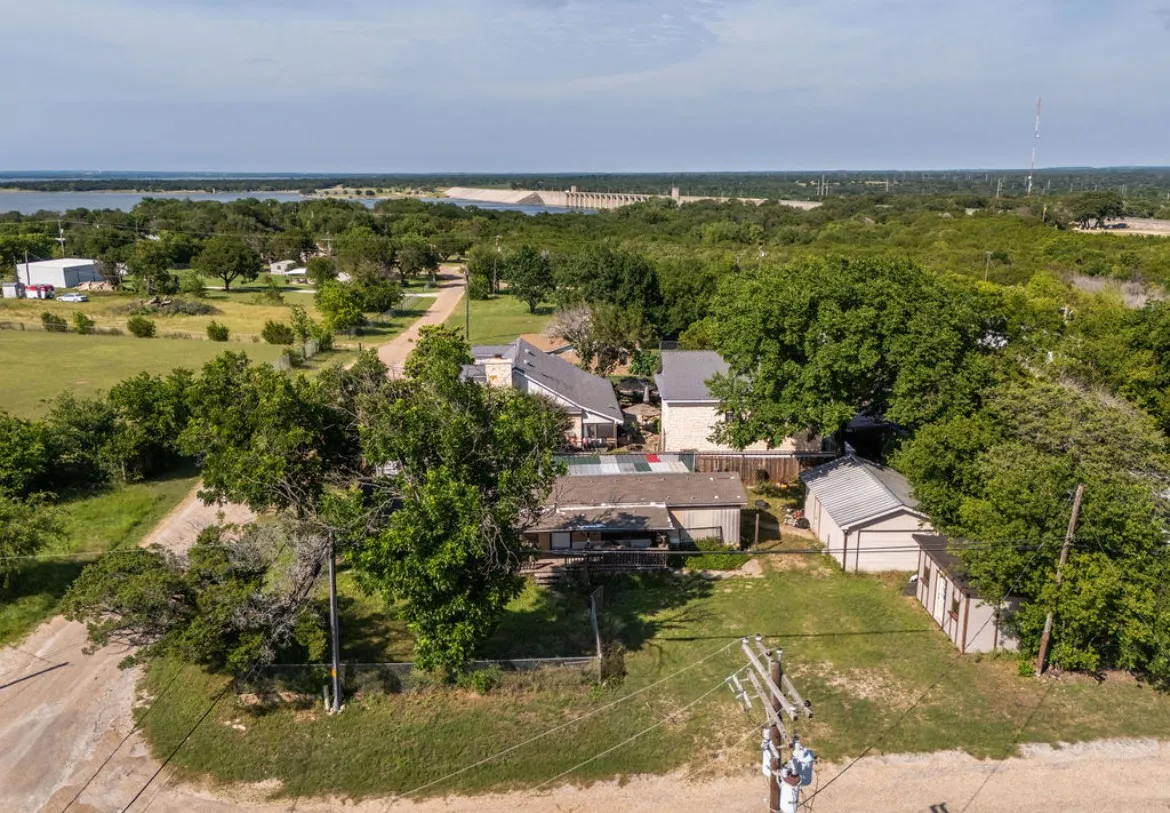 Aerial perspective showcasing a residential property with a main dwelling, an accessory structure, and a detached garage, all surrounded by mature trees