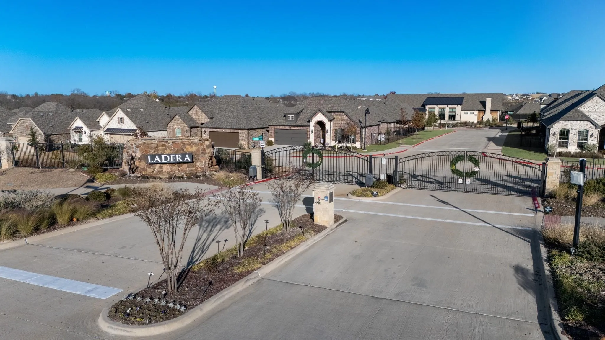 Gated community entrance featuring stone pillars, decorative wrought iron gates, and a prominent stone monument with property signage