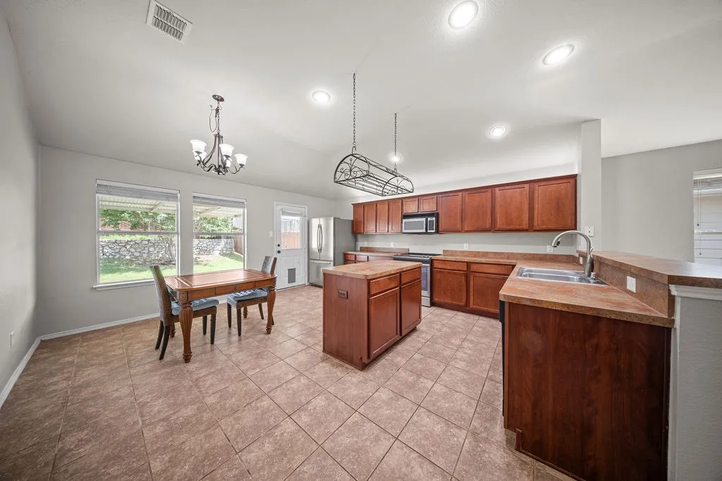 Spacious kitchen featuring a central island, ample wood cabinetry, light-toned tile flooring, and recessed lighting