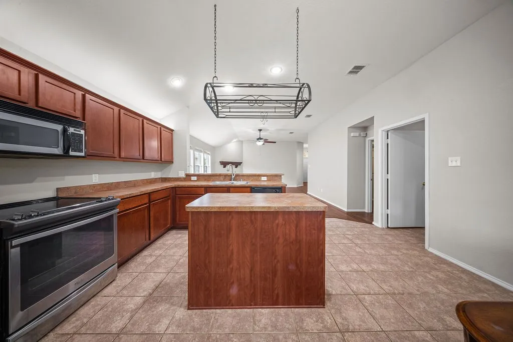 Kitchen featuring wood-finish cabinetry, a central island, stainless steel range and microwave, and tiled flooring